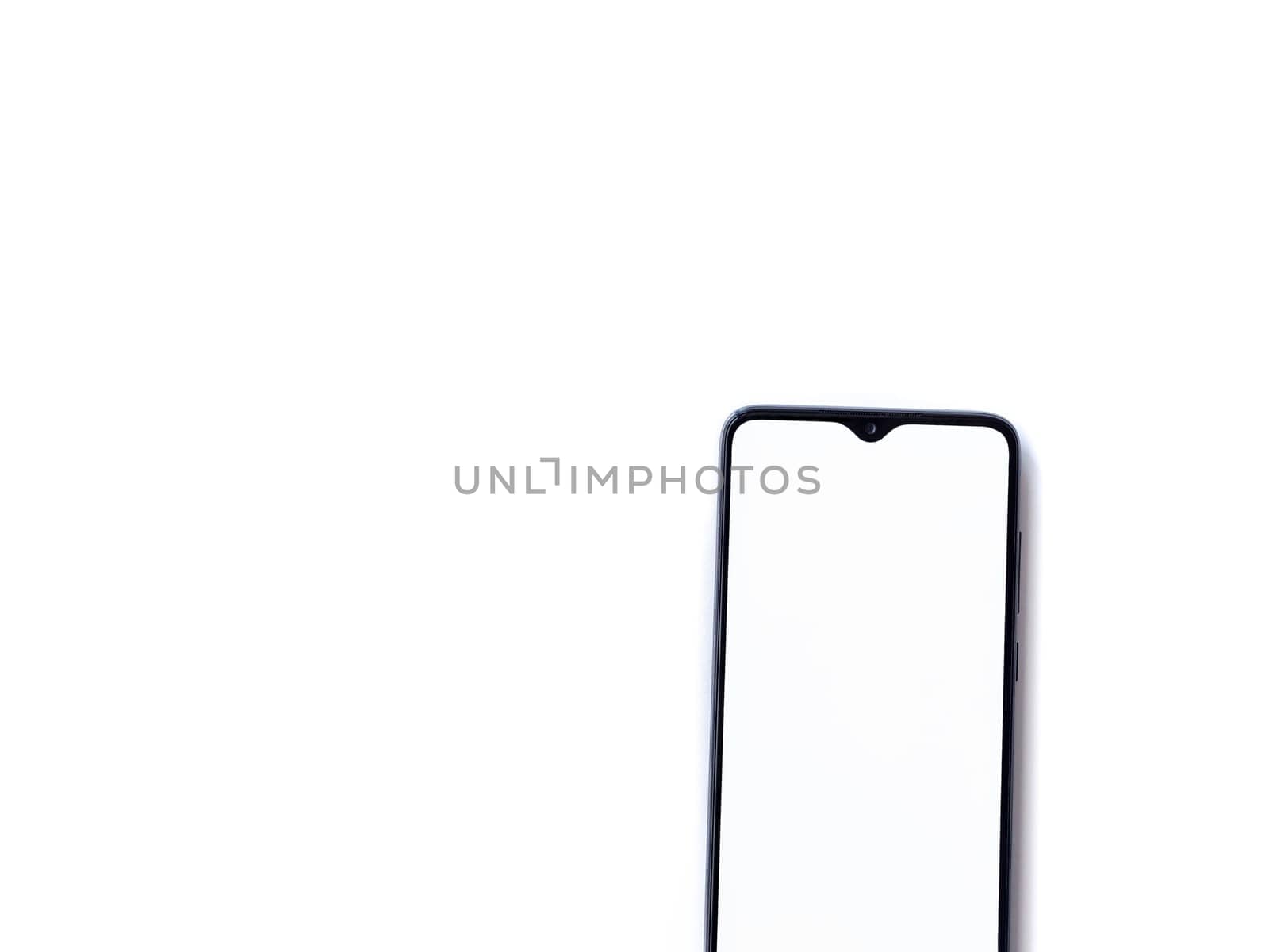 Black mobile smartphone mockup lies on the surface with blank screen isolated on white background. Top view flat lay with copy space, cut in the middle.
