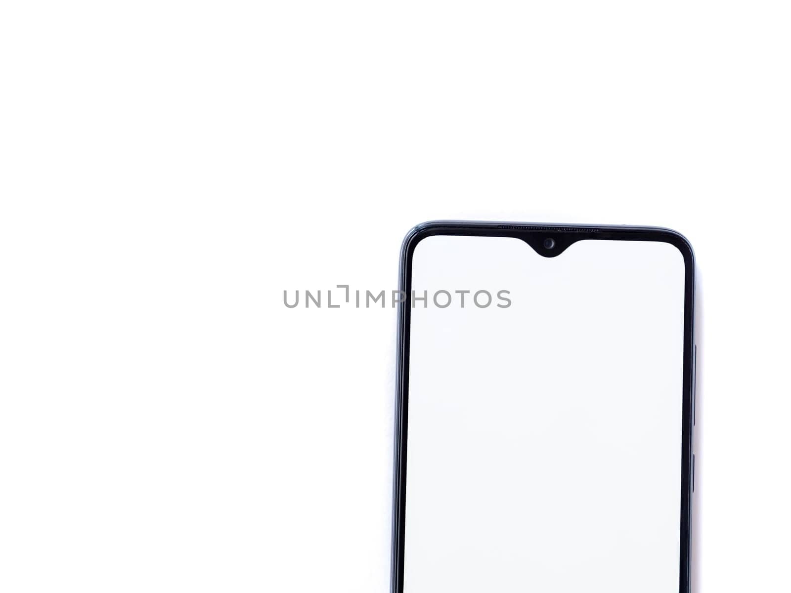 Black mobile smartphone mockup lies on the surface with blank screen isolated on white background. Top view flat lay with copy space, cut in the middle.