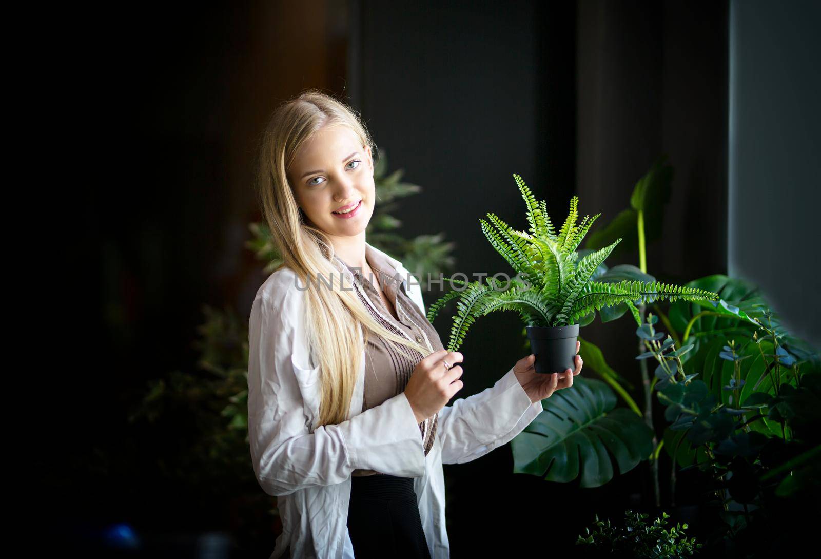 Caucasian young woman holding plants with green leaves at home. Home gardening.