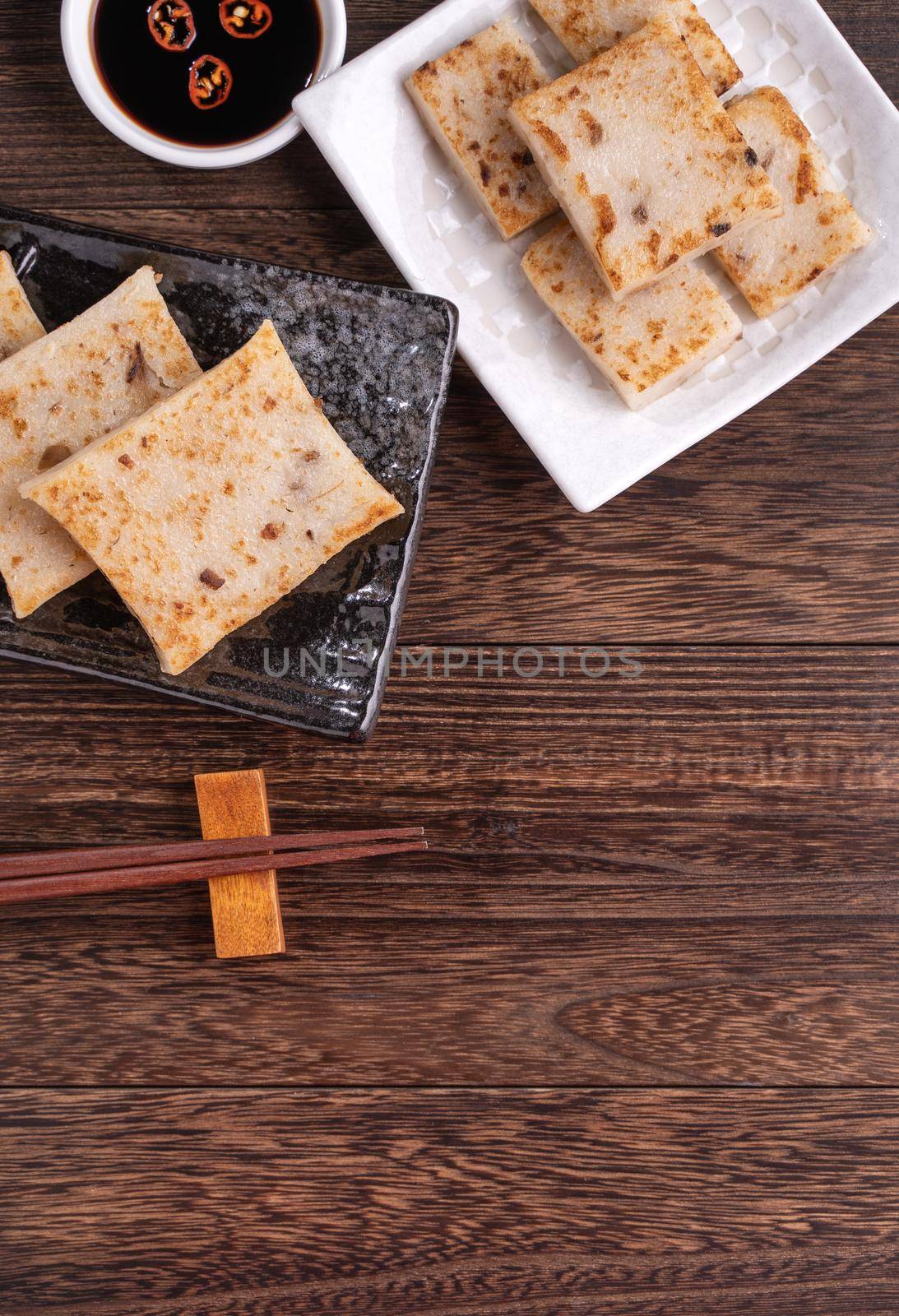 Delicious turnip cake, Chinese traditional local radish cake in restaurant with soy sauce and chopsticks, close up, copy space, top view, flat lay.