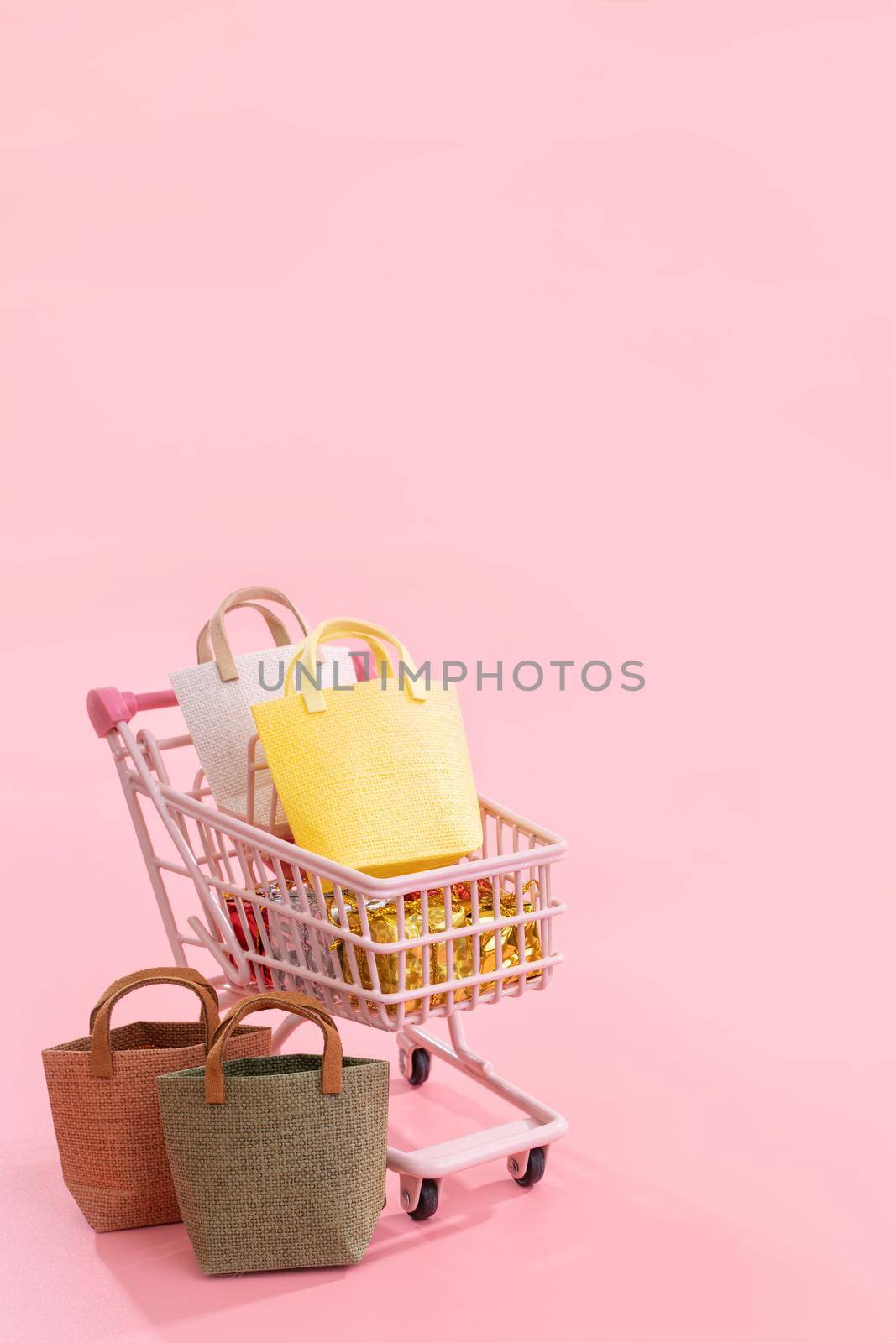 Annual sale shopping season concept - mini pink shop cart trolley full of paper bag gift isolated on pale pink background, blank copy space, close up