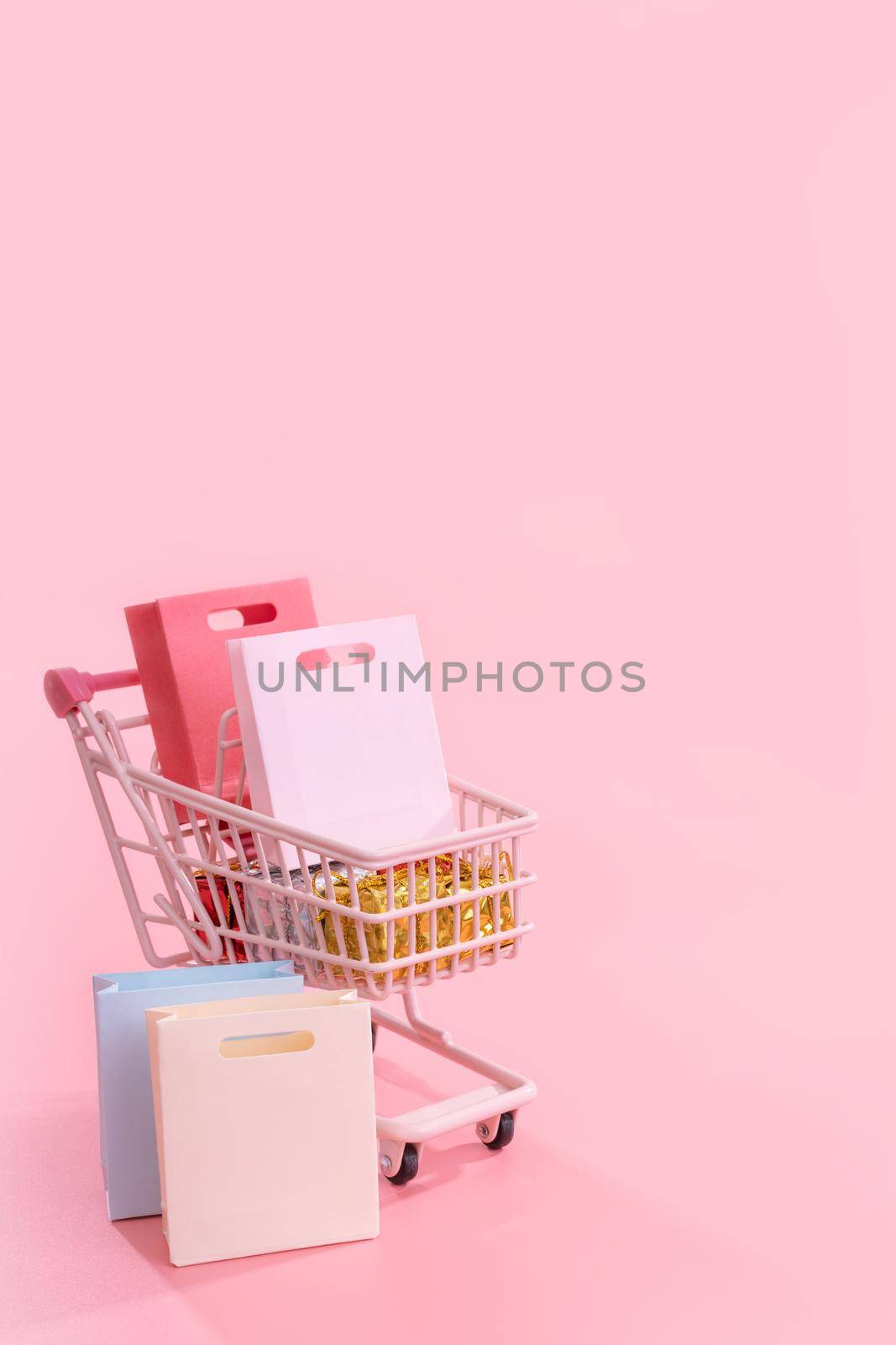 Annual sale shopping season concept - mini pink shop cart trolley full of paper bag gift isolated on pale pink background, blank copy space, close up