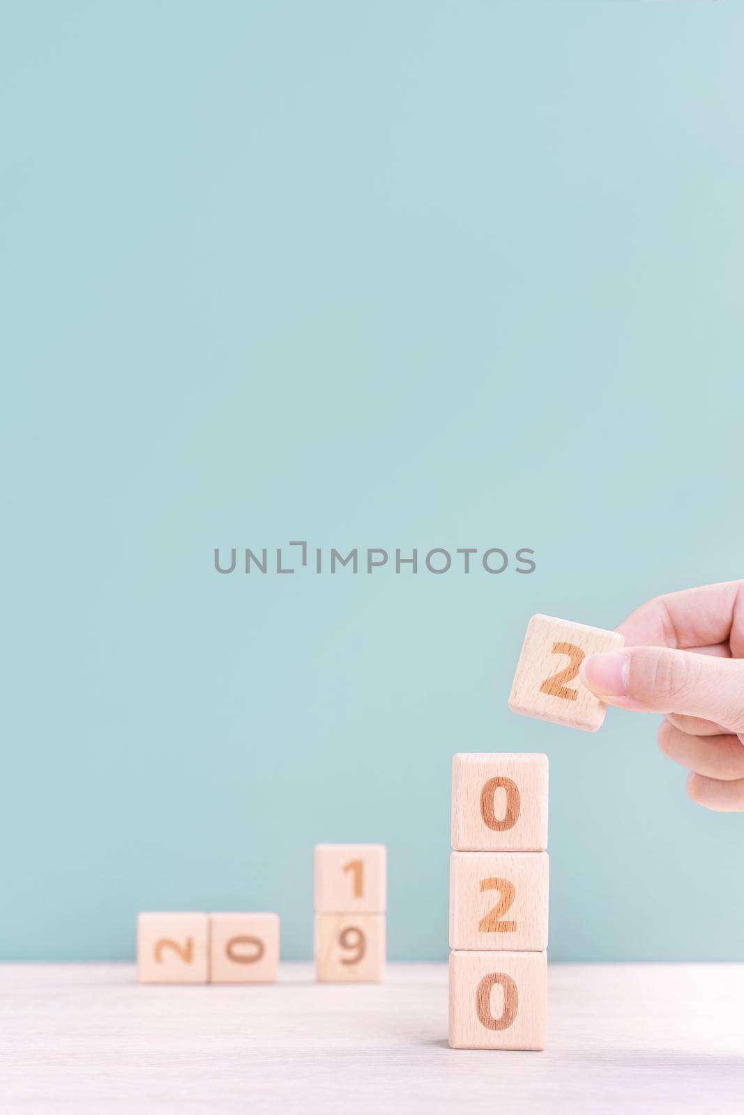 Abstract 2020 & 2019 New year countdown design concept - woman holding wood blocks cubes on wooden table and green background, close up, copy space.