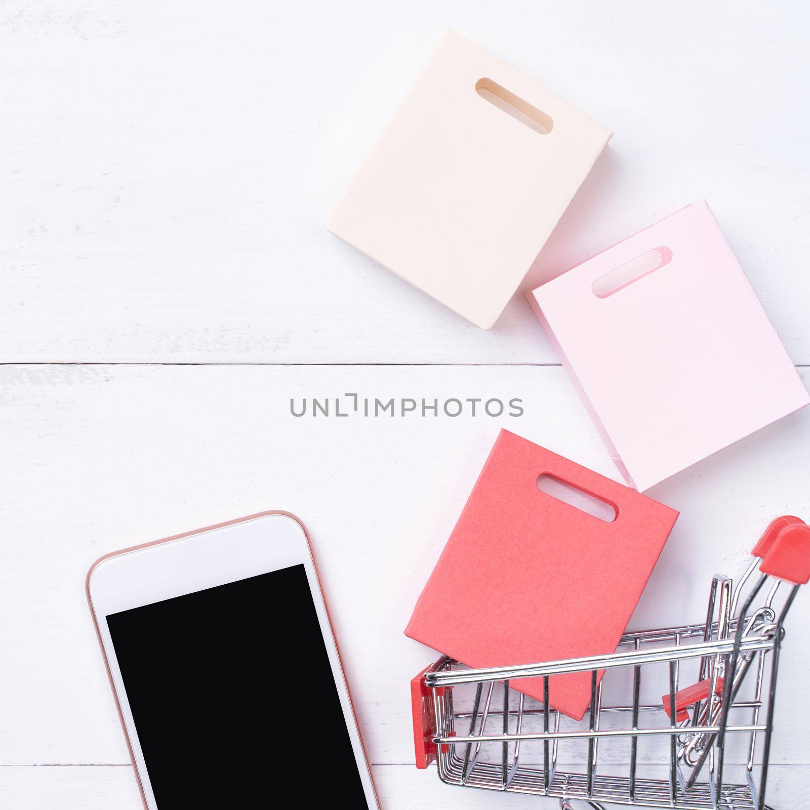 Abstract online shopping, mobile payment concept design element, colorful cart and paper bags on white wooden table background, top view, flat lay
