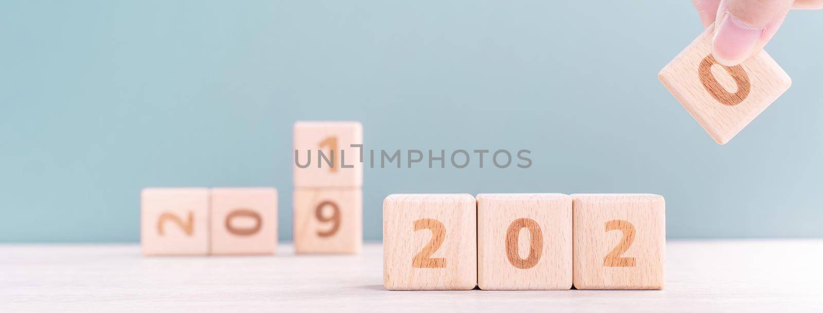 Abstract 2020 & 2019 New year countdown design concept - woman holding wood blocks cubes on wooden table and green background, close up, copy space. by ROMIXIMAGE