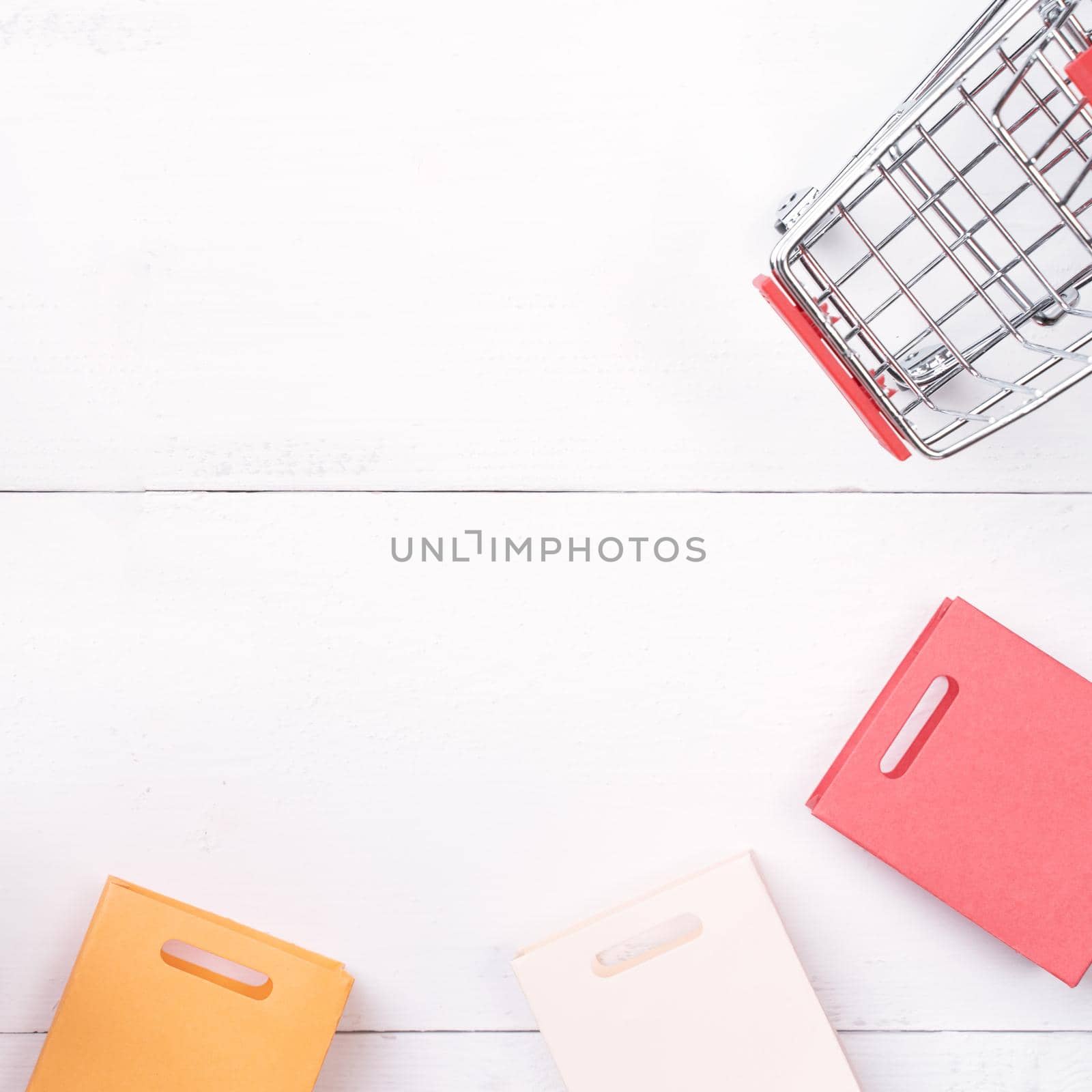 Abstract design element,annual sale,shopping season concept,mini cart with colorful paper bag on white wooden table background,top view,flat lay