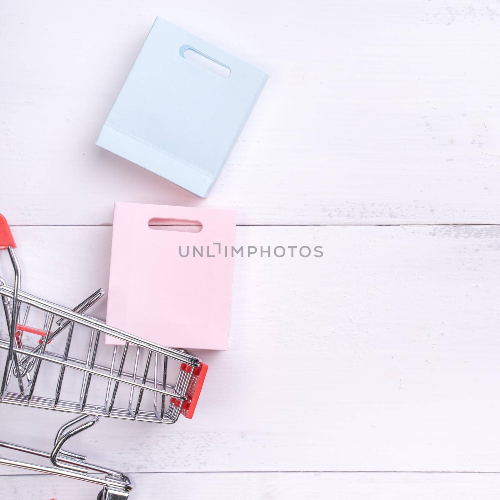 Abstract design element,annual sale,shopping season concept,mini cart with colorful paper bag on white wooden table background,top view,flat lay