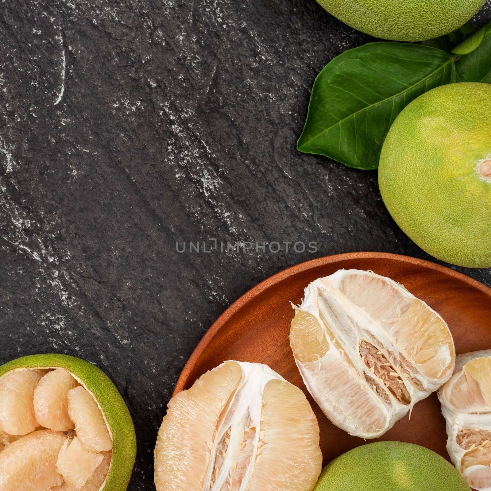 Fresh pomelo,grapefruit in bamboo basket with green leaf on dark black slate background. Seasonal fruit for Mid-Autumn Festival. Top view. Flat lay.
