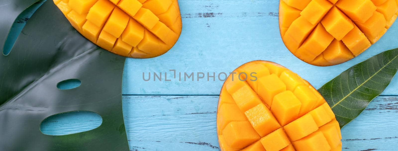 Fresh mango, beautiful chopped fruit with green leaves on dark wooden table background. Tropical fruit design concept. Flat lay. Top view. Copy space