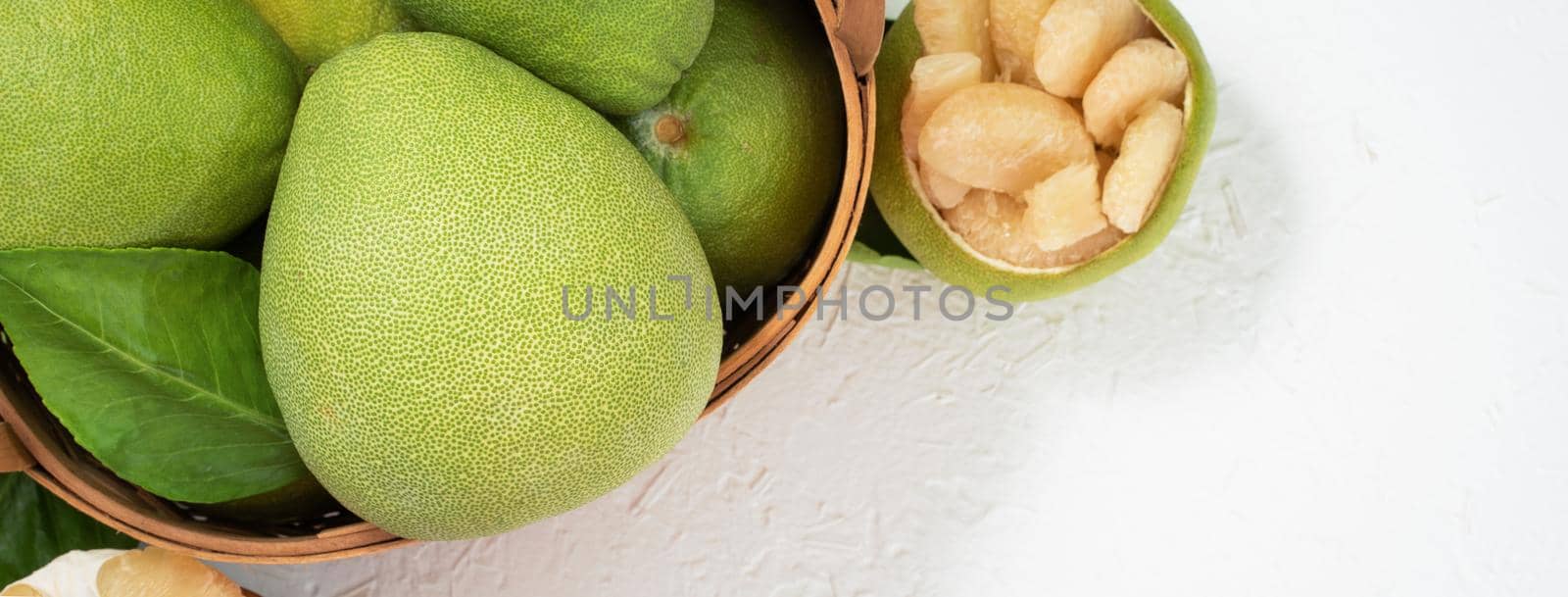 Fresh pomelo, grapefruit in bamboo basket with green leaf on bright white background. Seasonal fruit for Mid-Autumn Festival. Top view. Flat lay. by ROMIXIMAGE