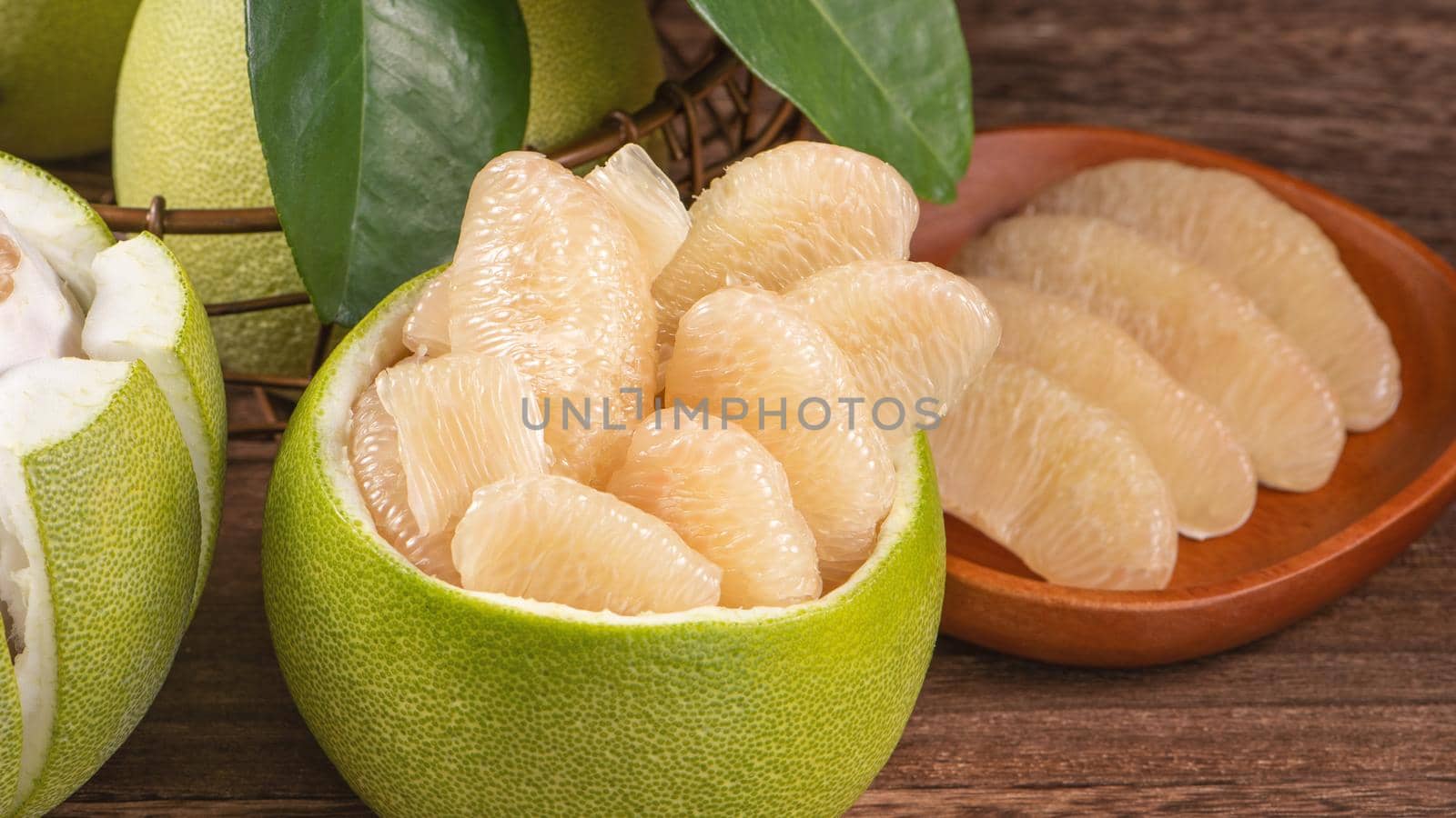 Fresh peeled pomelo, grapefruit, shaddock with green leaves on dark wooden plank table. Seasonal fruit near mid-autumn festival, close up, copy space