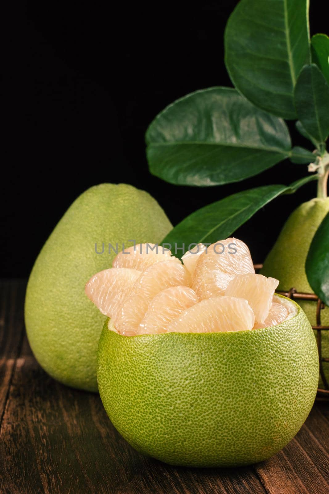 Fresh peeled pomelo, grapefruit, shaddock with green leaves on dark wooden plank table. Seasonal fruit near mid-autumn festival, close up, copy space