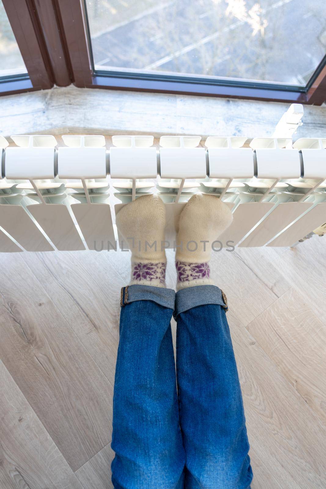 Woman warming up with feet on heater wearing woolen socks, view from above by Mariakray