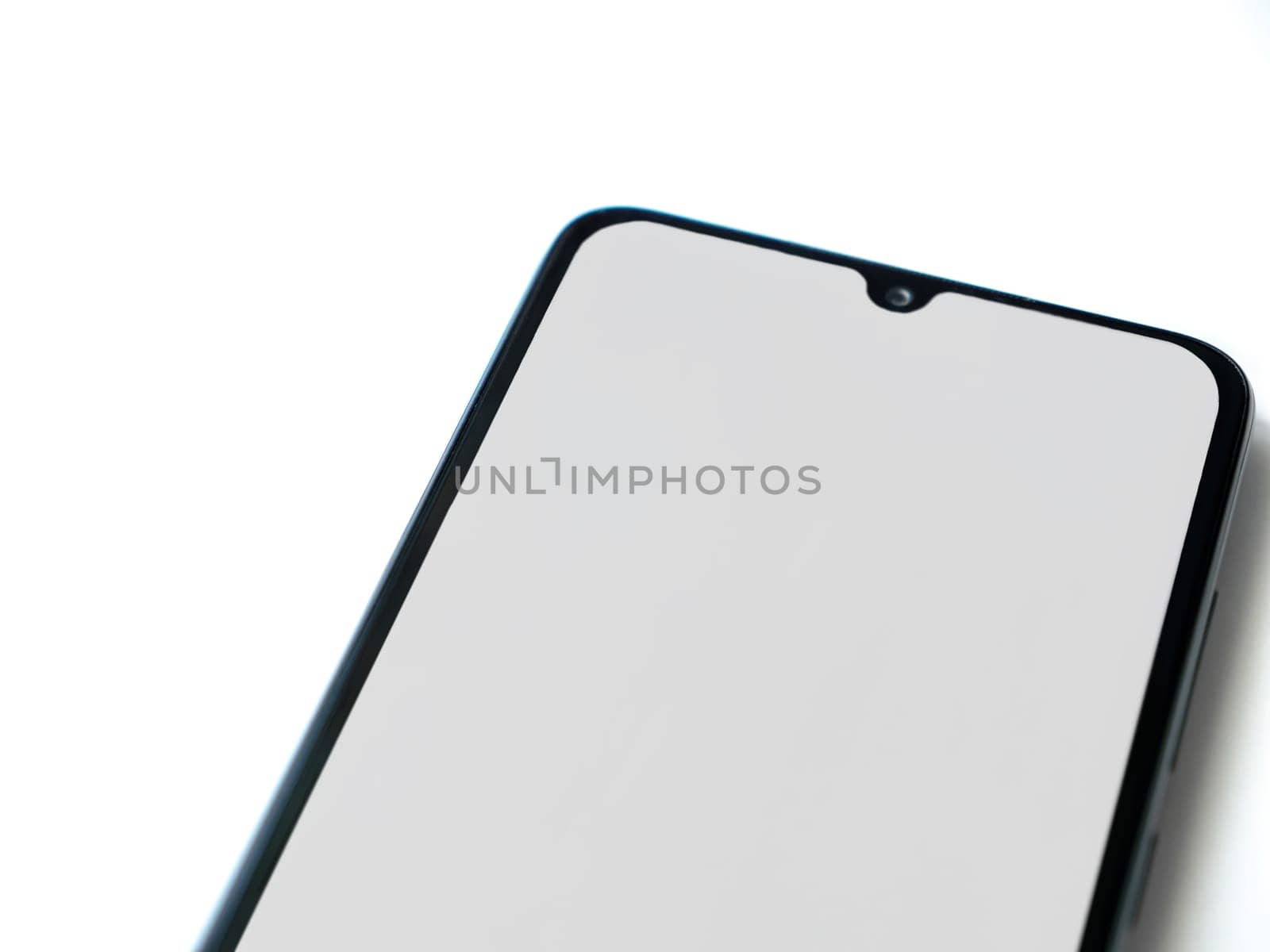 Black mobile smartphone mockup lies on the surface with blank screen isolated on white background. Top view closeup with selective focus and copy space, cut in the middle.