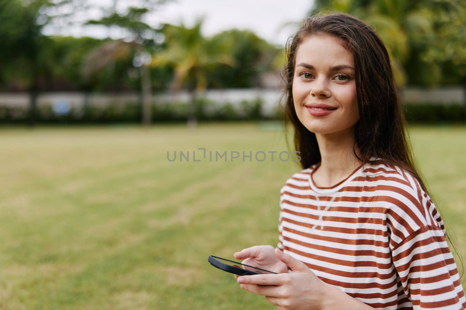 talk woman adult grass bag caucasian talking human striped jeans happy walk phone blogger tree palm park working smiling lifestyle network nature