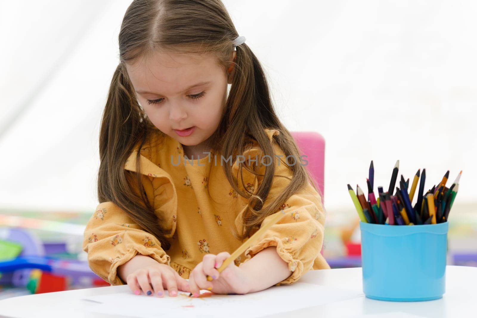 Cute young european kid girl painting with colored pencil. Kindergarten children education concept.