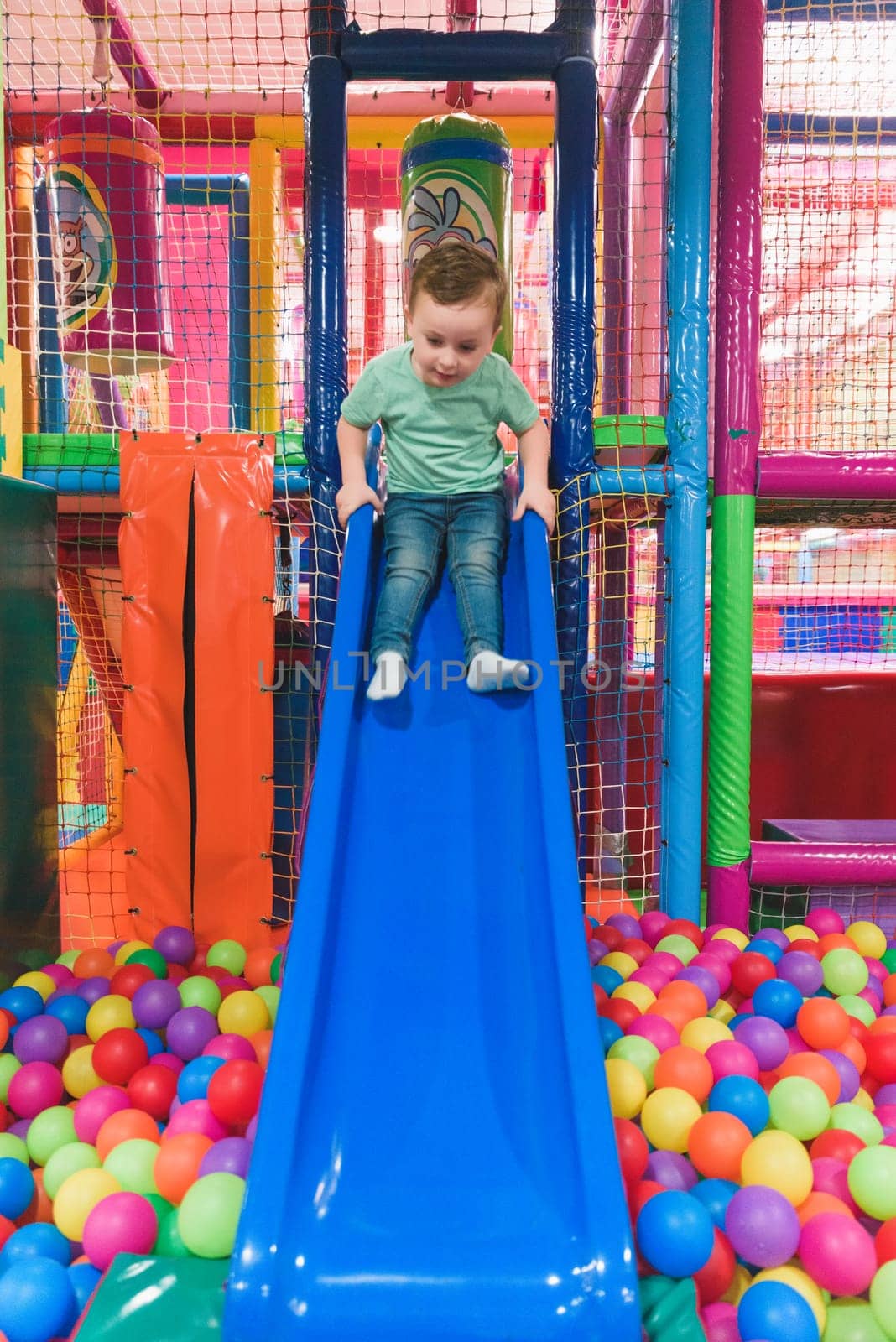 Cheerful boy playing in slide and pool with colorful balls.