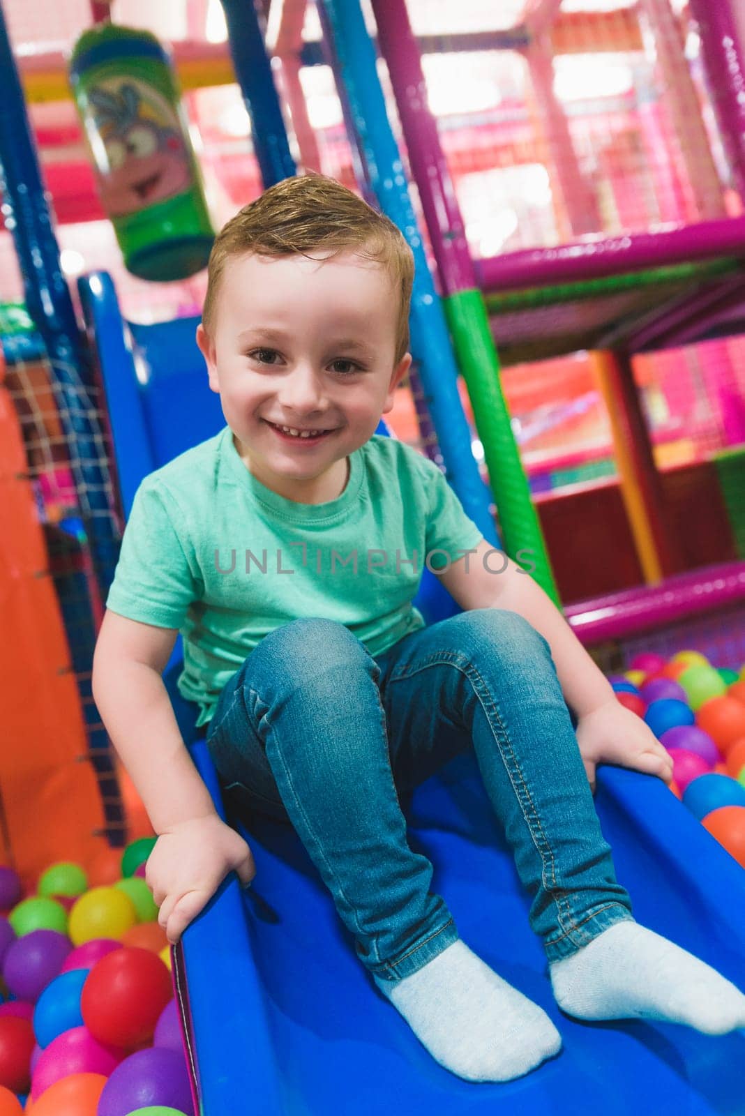 Cheerful boy playing in slide and pool with colorful balls.