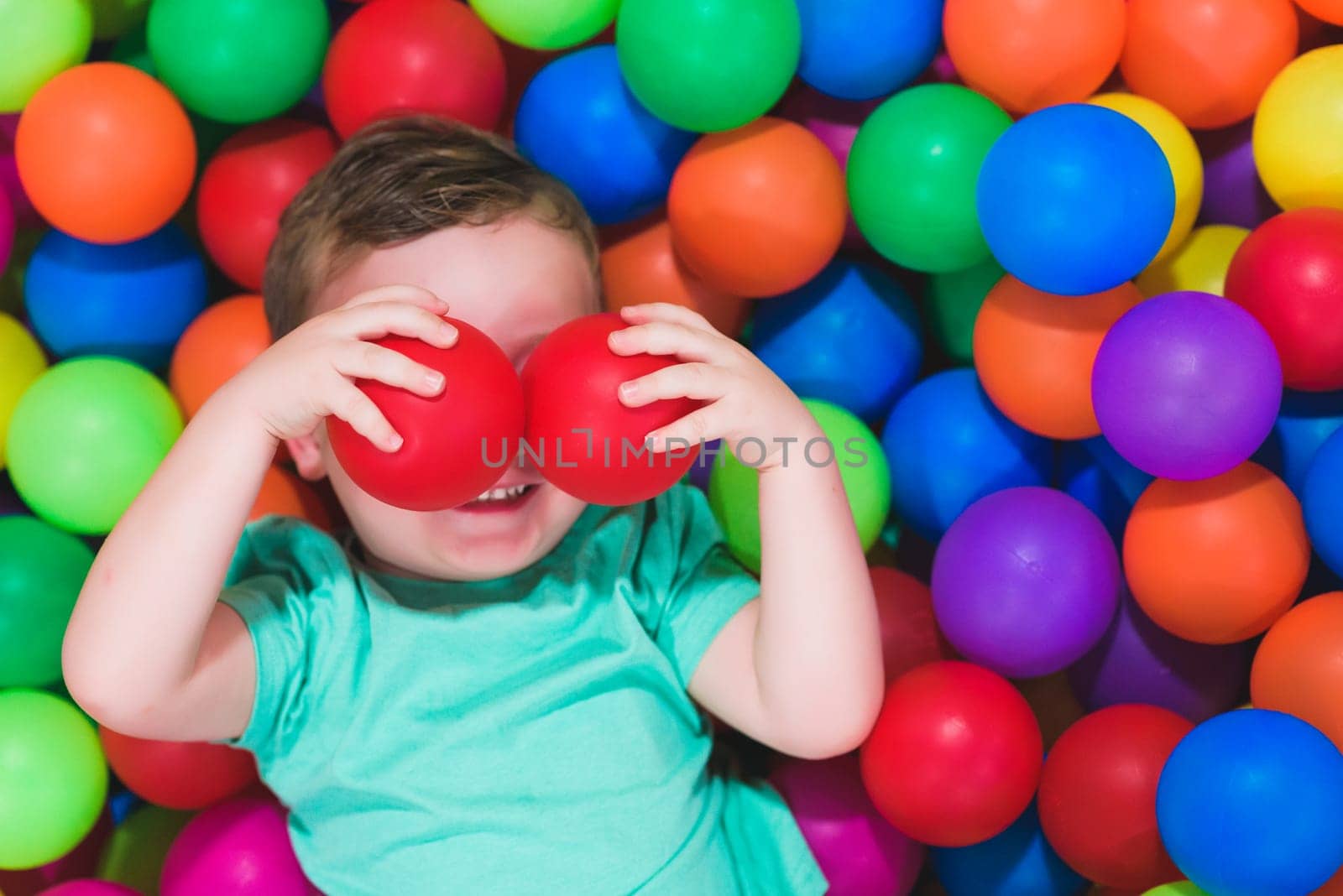 Portrait of funny little boy playing in ball pit and enjoying time in children's play and entertainment area, copy space.