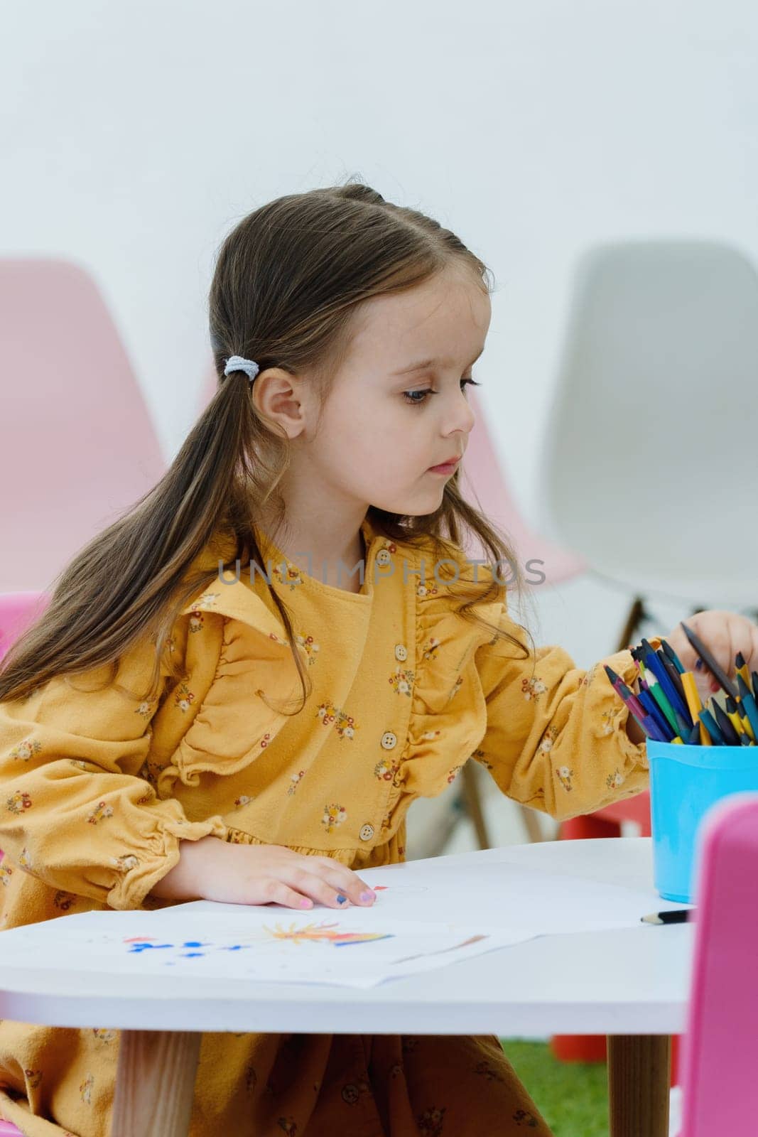 Cute european kid girl painting with colored pencil. Kindergarten children education concept.