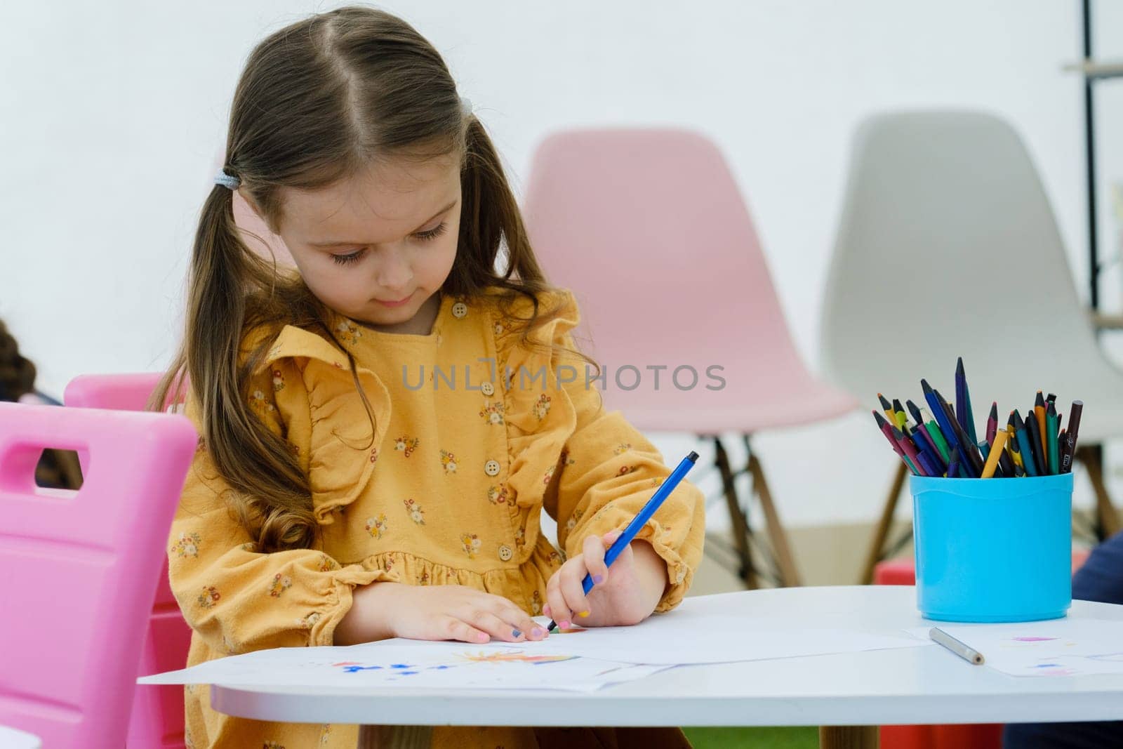 Kid girl painting with colored pencil. Kindergarten children education concept. by leonik