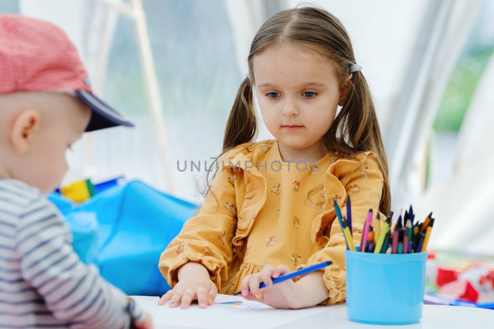 Kid girl painting with colored pencil. Kindergarten children education concept.