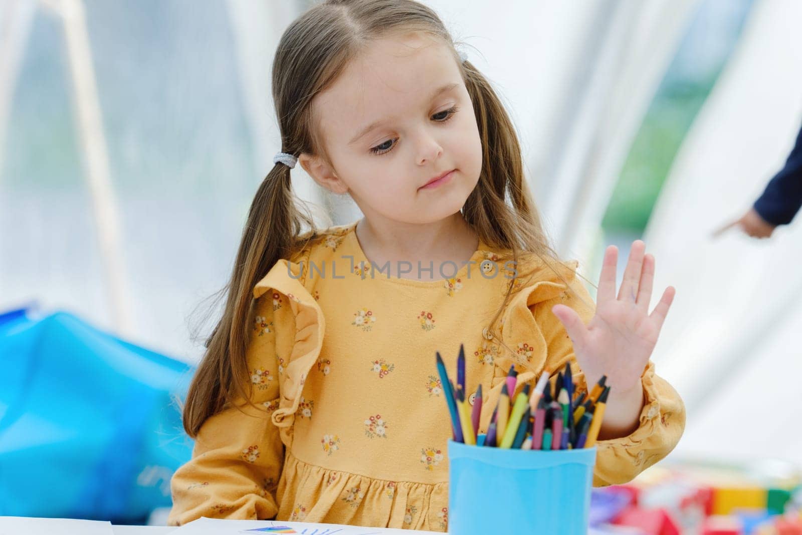 Cute european kid girl painting with colored pencil. Kindergarten children education concept.