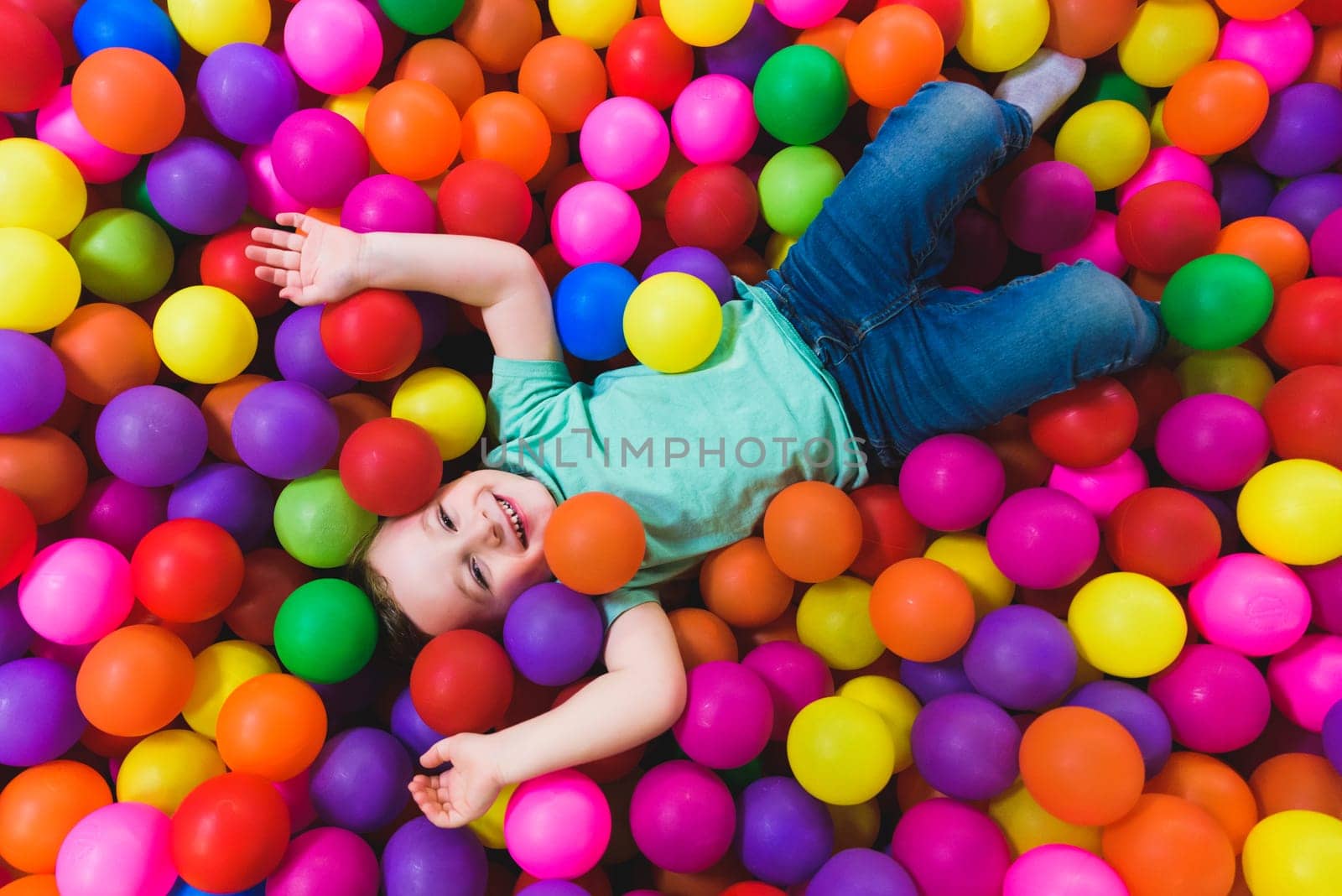 Smiling boy playing lying on colorful balls in the park by jcdiazhidalgo