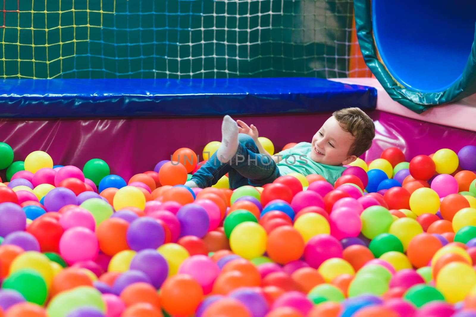 Happy laughing child laughing in an indoor play center. Children playing with colored balls in the playground ball pool. Party.