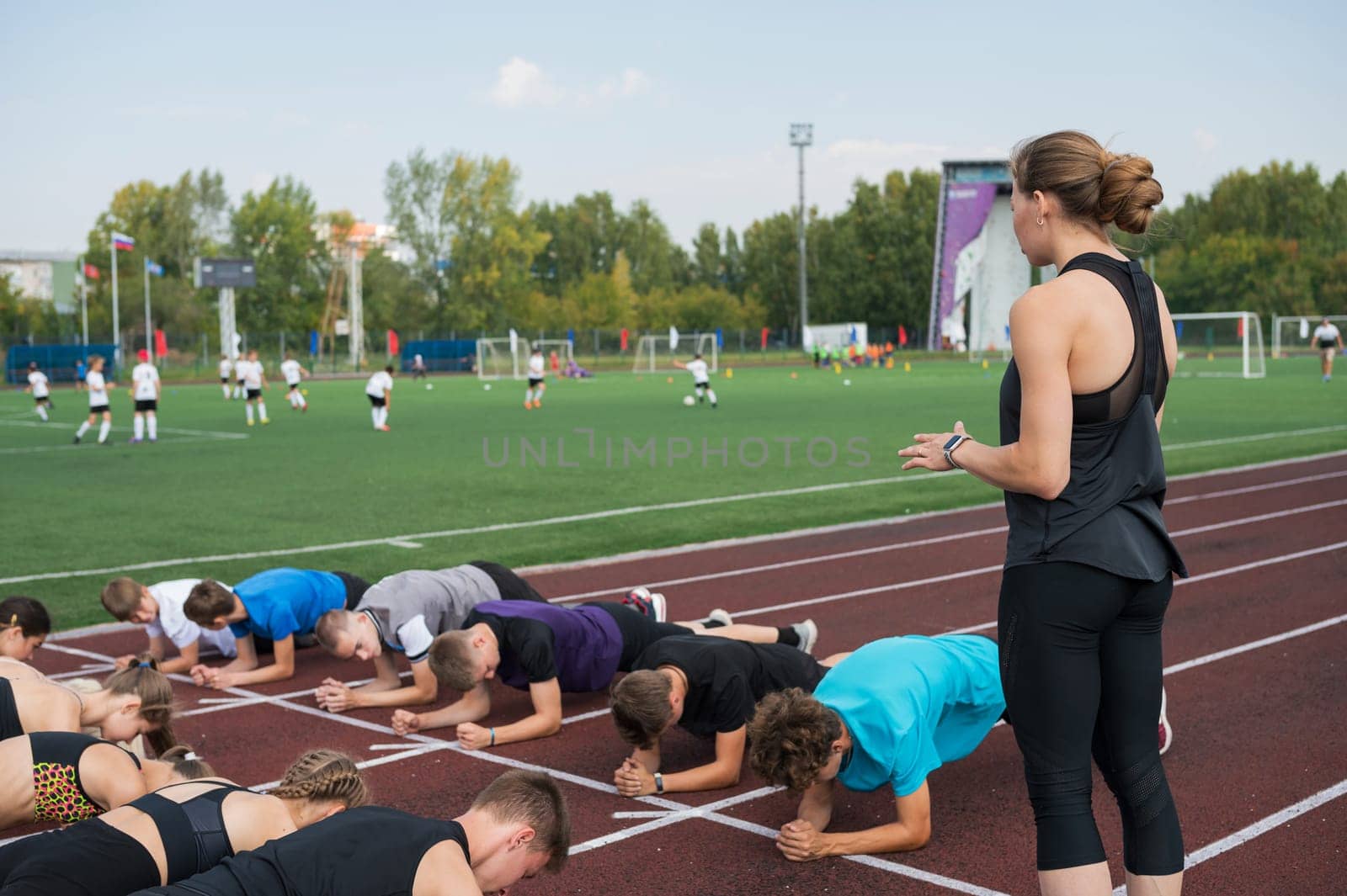 Female coach and group of children conducts a training session at the stadium. School gym trainings or athletics