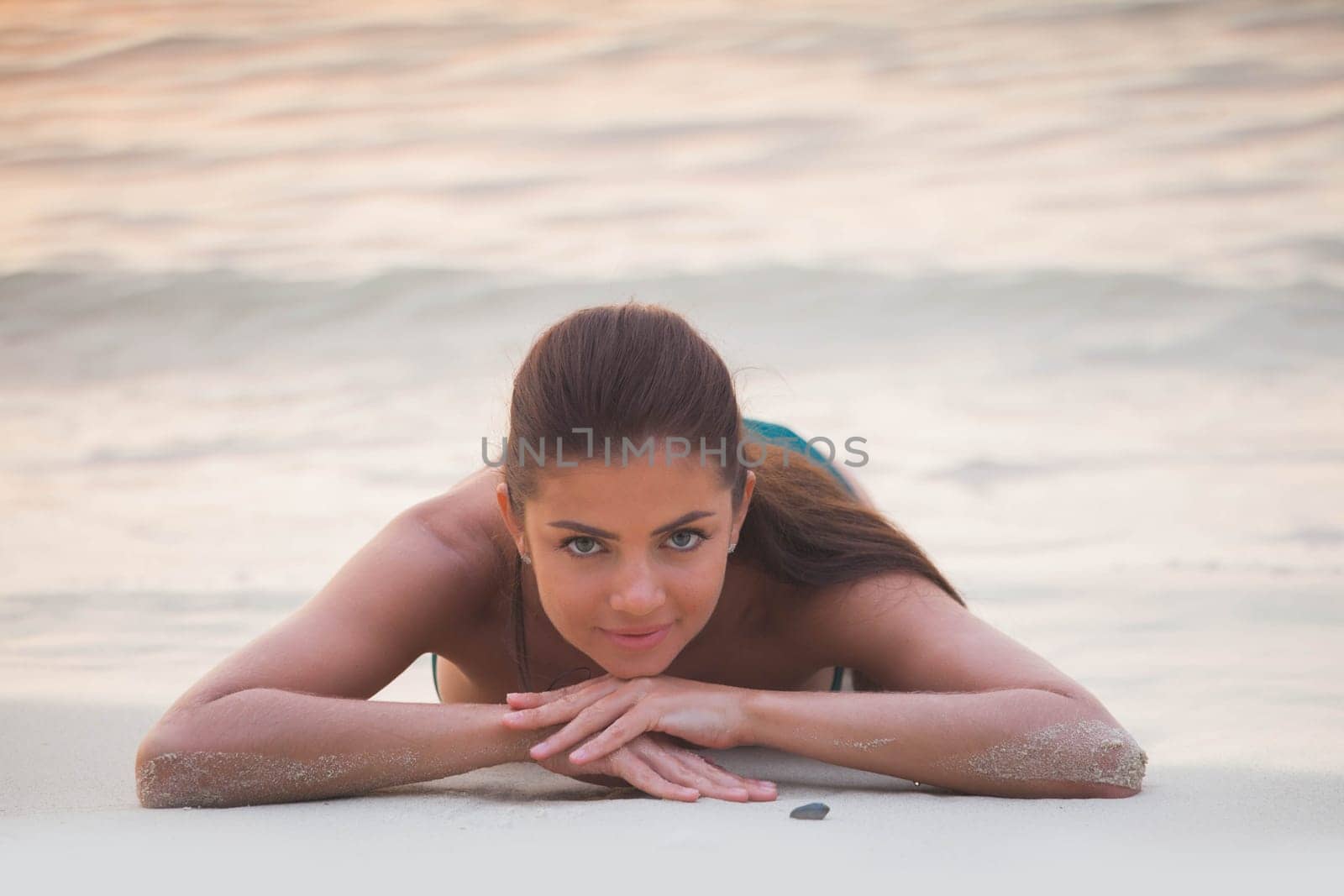 Beautiful woman lays on sand of beach in sunset