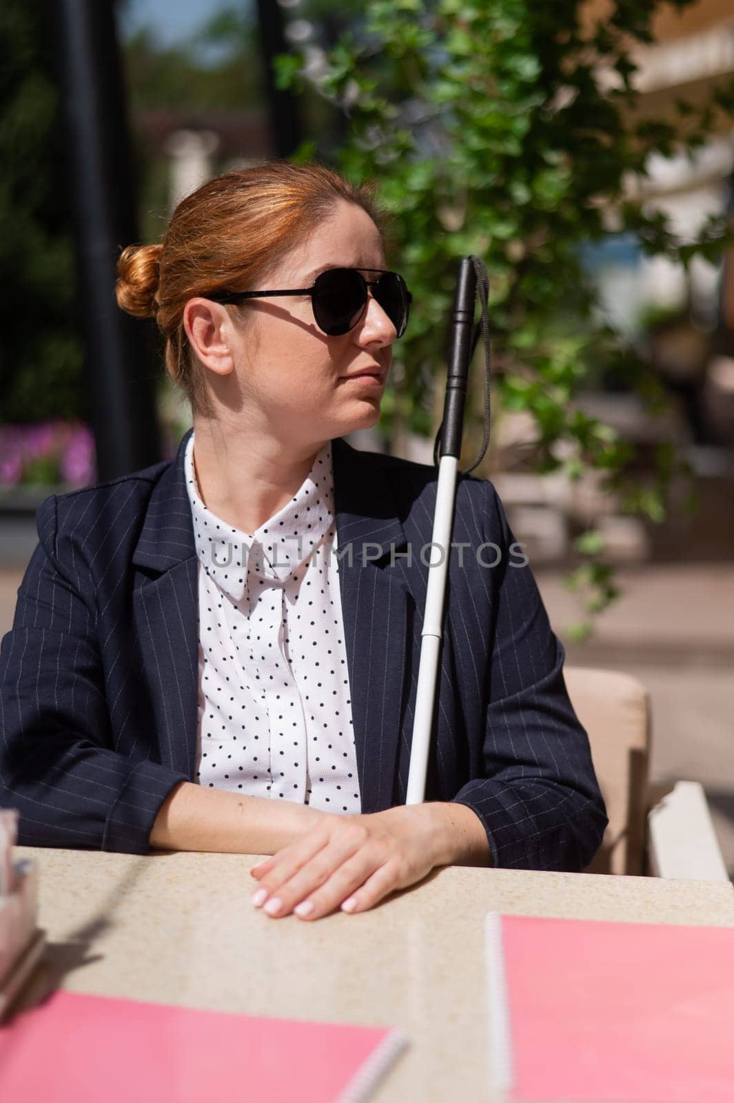 A blind woman in a business suit is sitting in an outdoor cafe