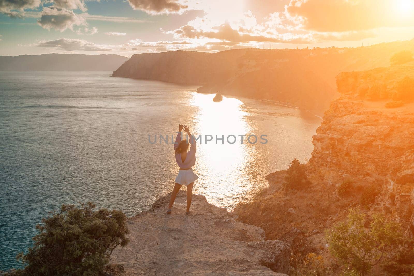 Free girl with open arms at sunset over the sea, sun over clouds by Matiunina