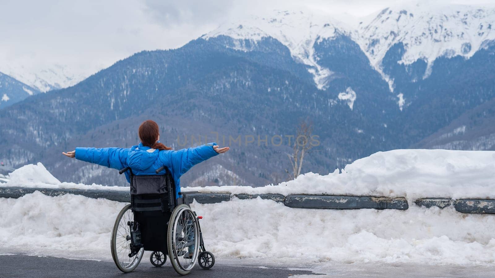 Rear view of a woman in a wheelchair spread her arms to the side like wings in the mountains in winter