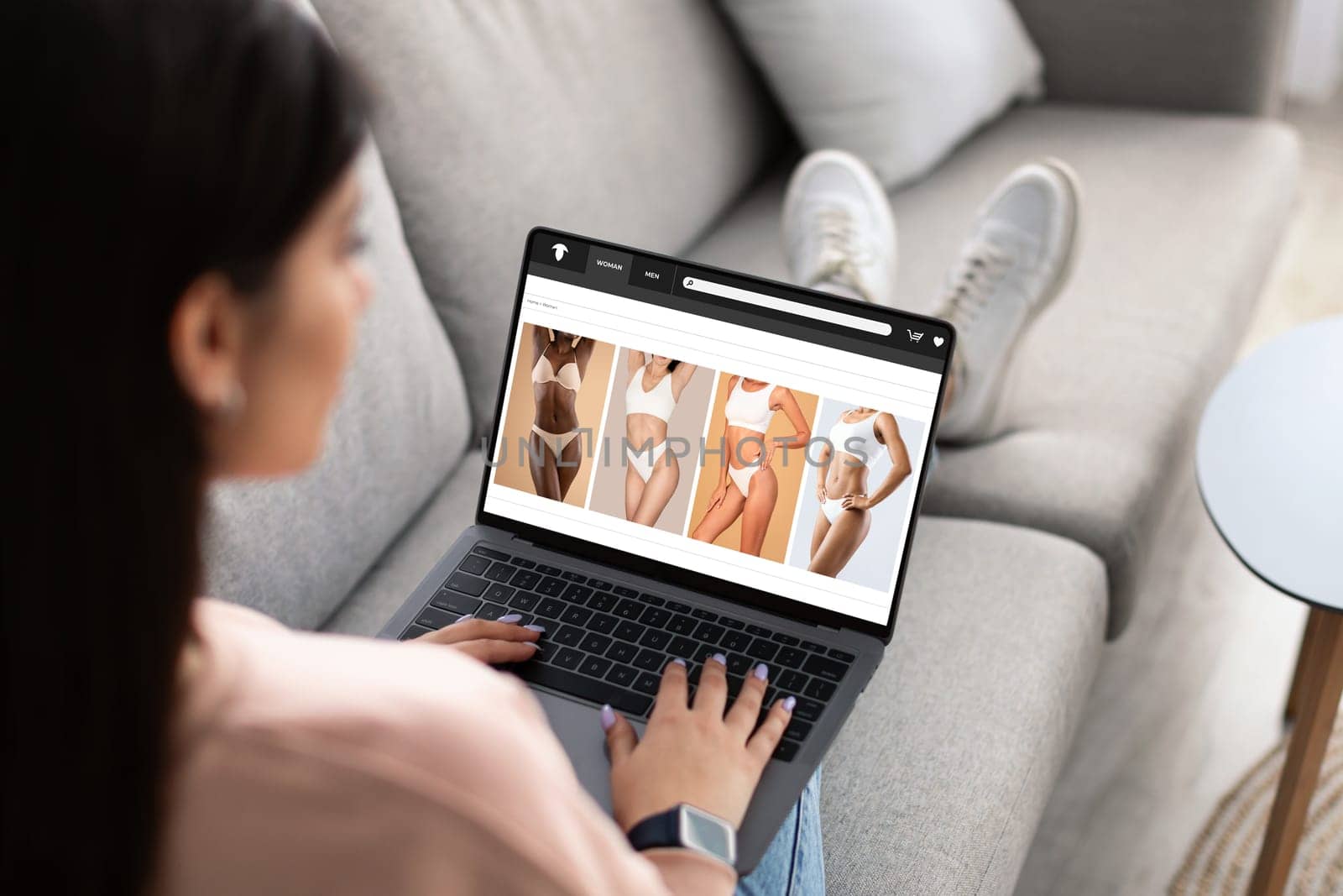Millennial arabic woman shopaholic enjoy online shopping, buy underwear on laptop screen, sitting on sofa in living room. Website, app for fashion, order delivery, sale at home