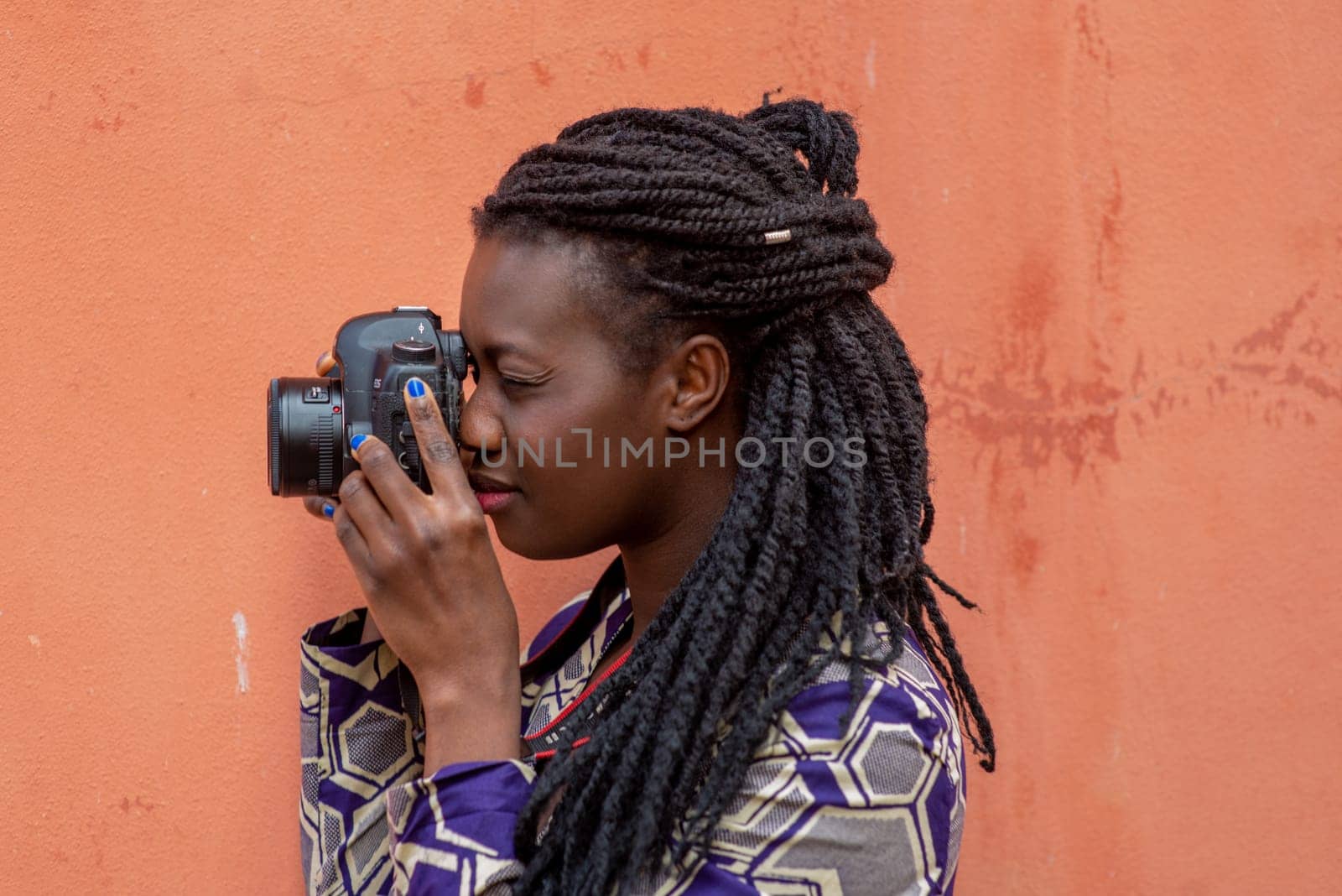 Close up portrait of beautiful young african american woman with braid hairstyle concentrated while making a photograph with reflex camera over a wall outdoors