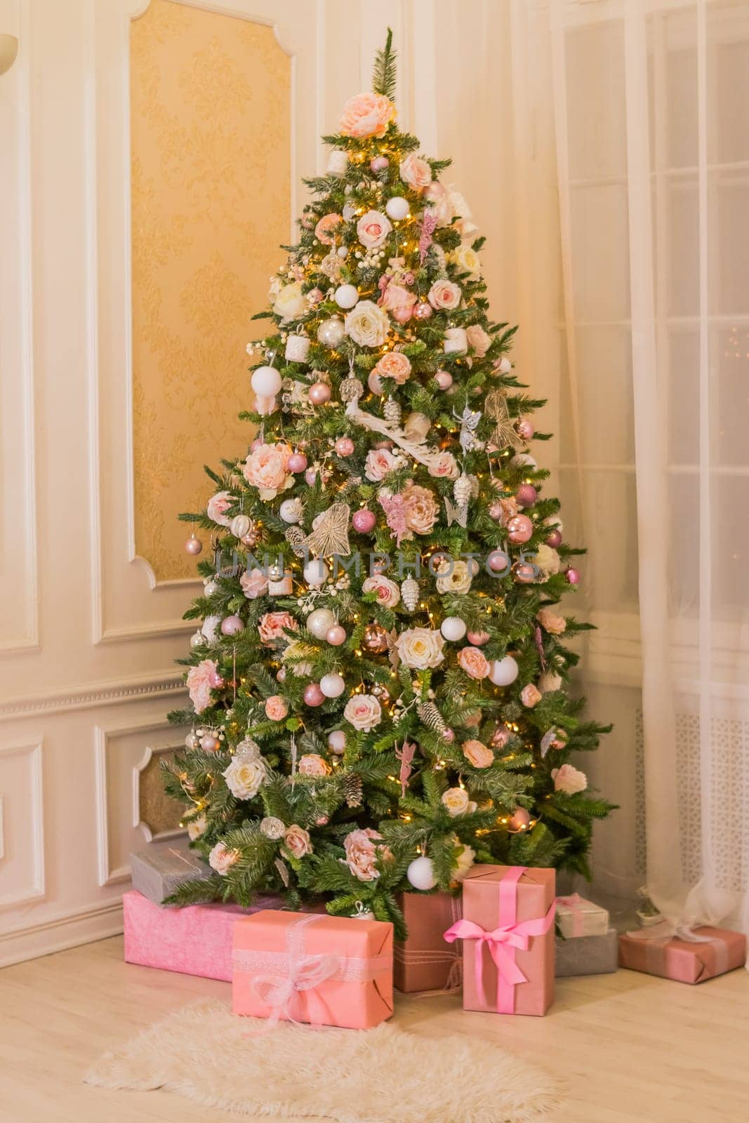 Pastel christmas.pinkChristmas gift box with golden ribbon next to decorated Christmas tree