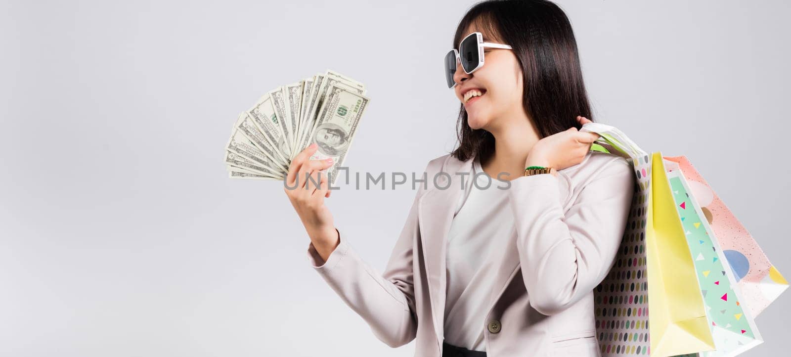 Woman with glasses confident shopper smile holding online shopping bags multicolor and dollar money banknotes on hand by Sorapop
