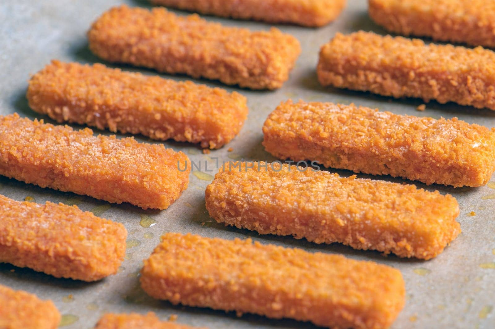 A lot of fish sticks ready for frying on special paper. Cooking concept for frying fish fingers in the oven. Side view. High quality photo