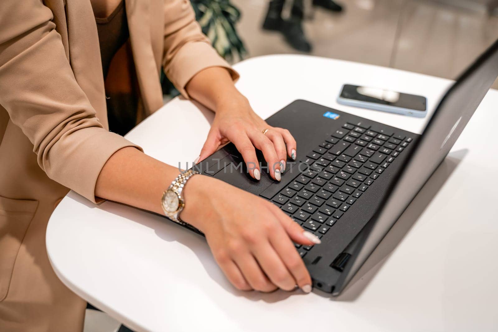 A business woman sits in a cafe and works at a computer. She is wearing a beige jacket