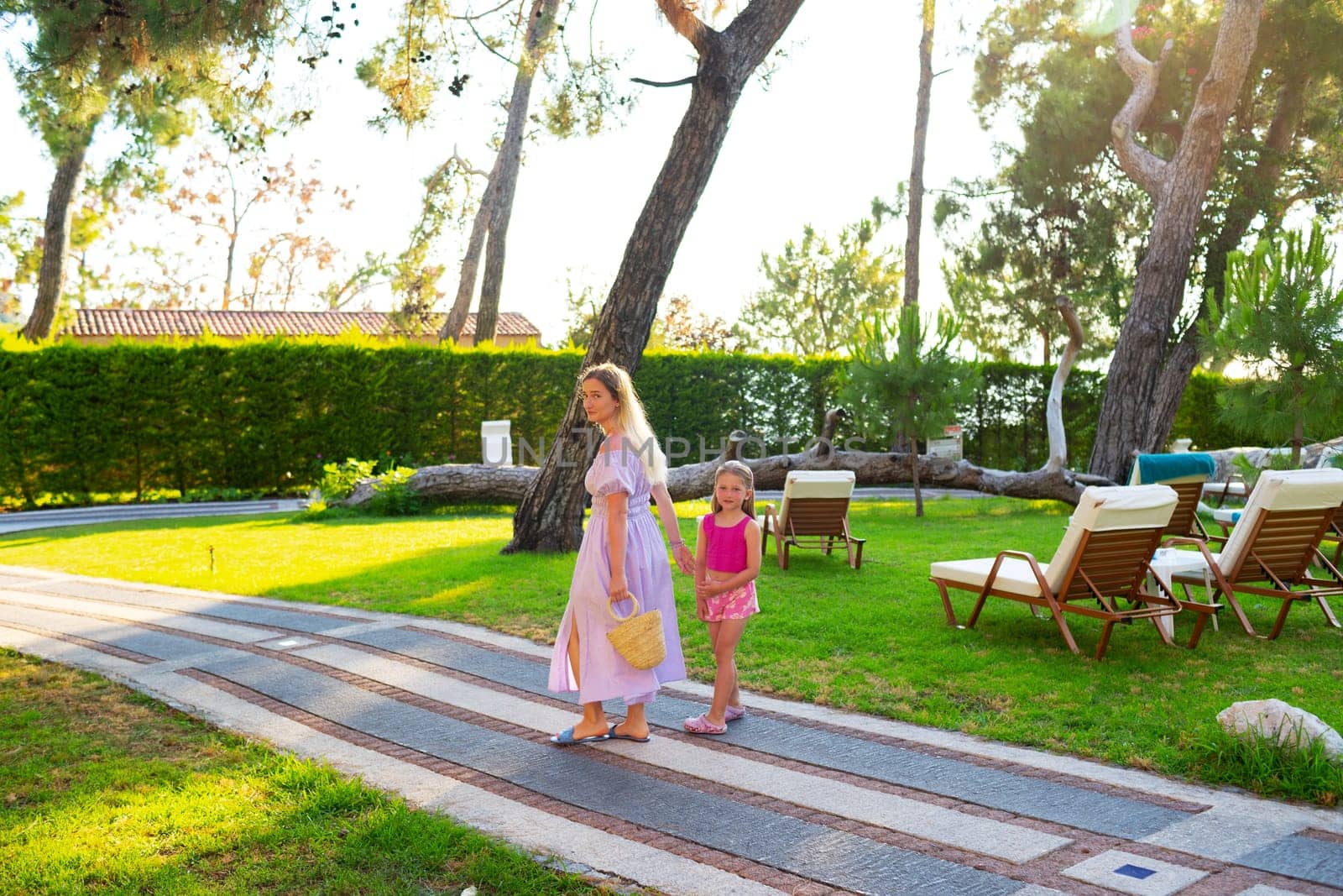 Mother and daughter enjoying walk outdoors in summer, back view