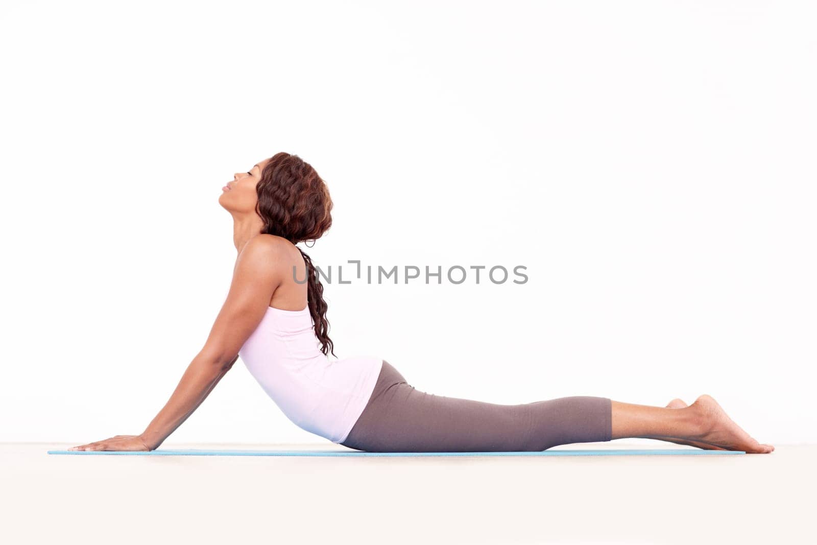 Yoga, cobra back stretch and black woman relax in studio on a fitness and workout mat for training. Isolated, white background and calm African female person lying on the ground with body stretching by YuriArcurs