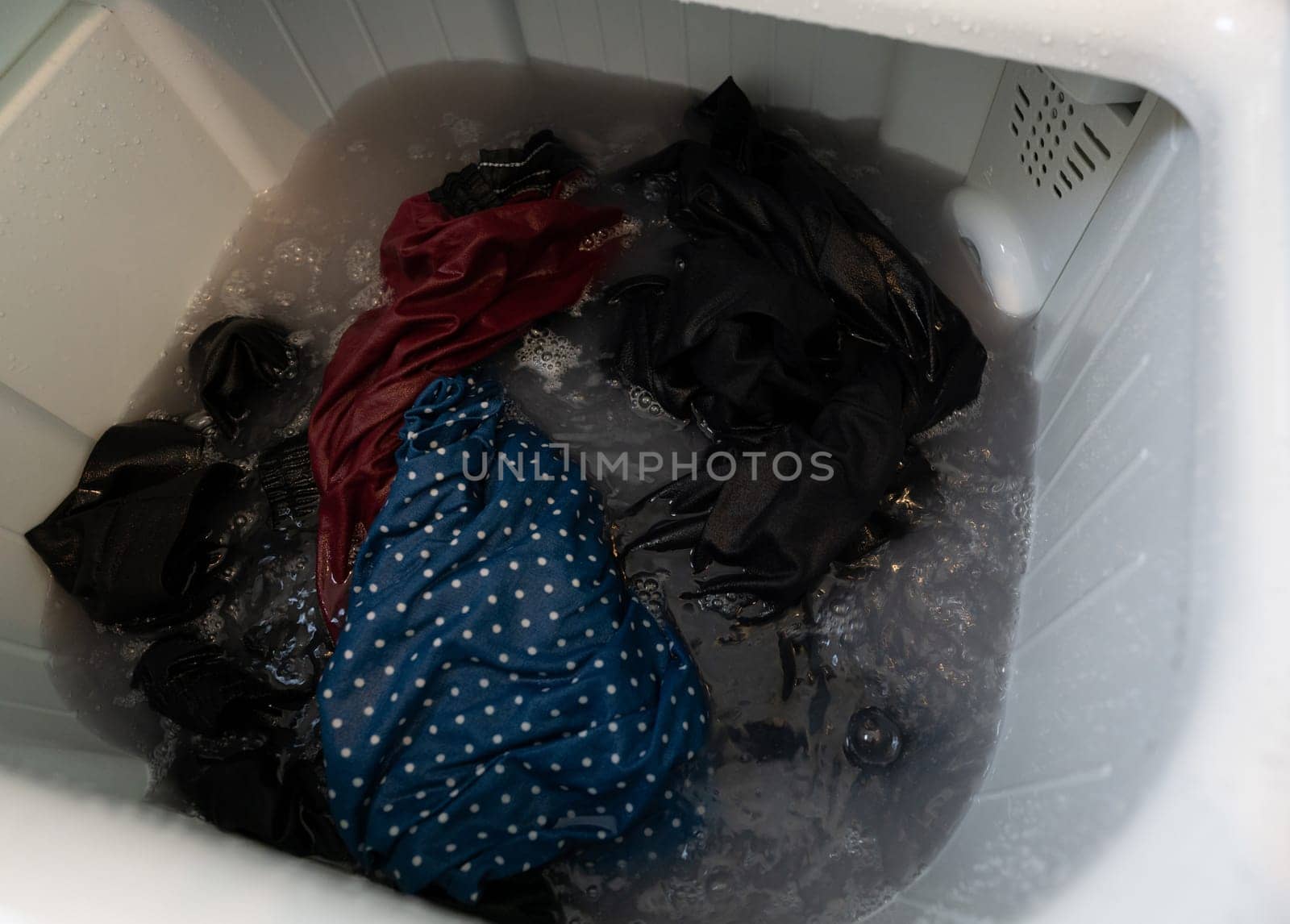 Dirty clothes in top loading washing machine. Clothes with bubble of laundry detergent in washing machine. Laundry concept. Top load washer. Housework. Washing machine and dirty water from cleaning. by Fahroni
