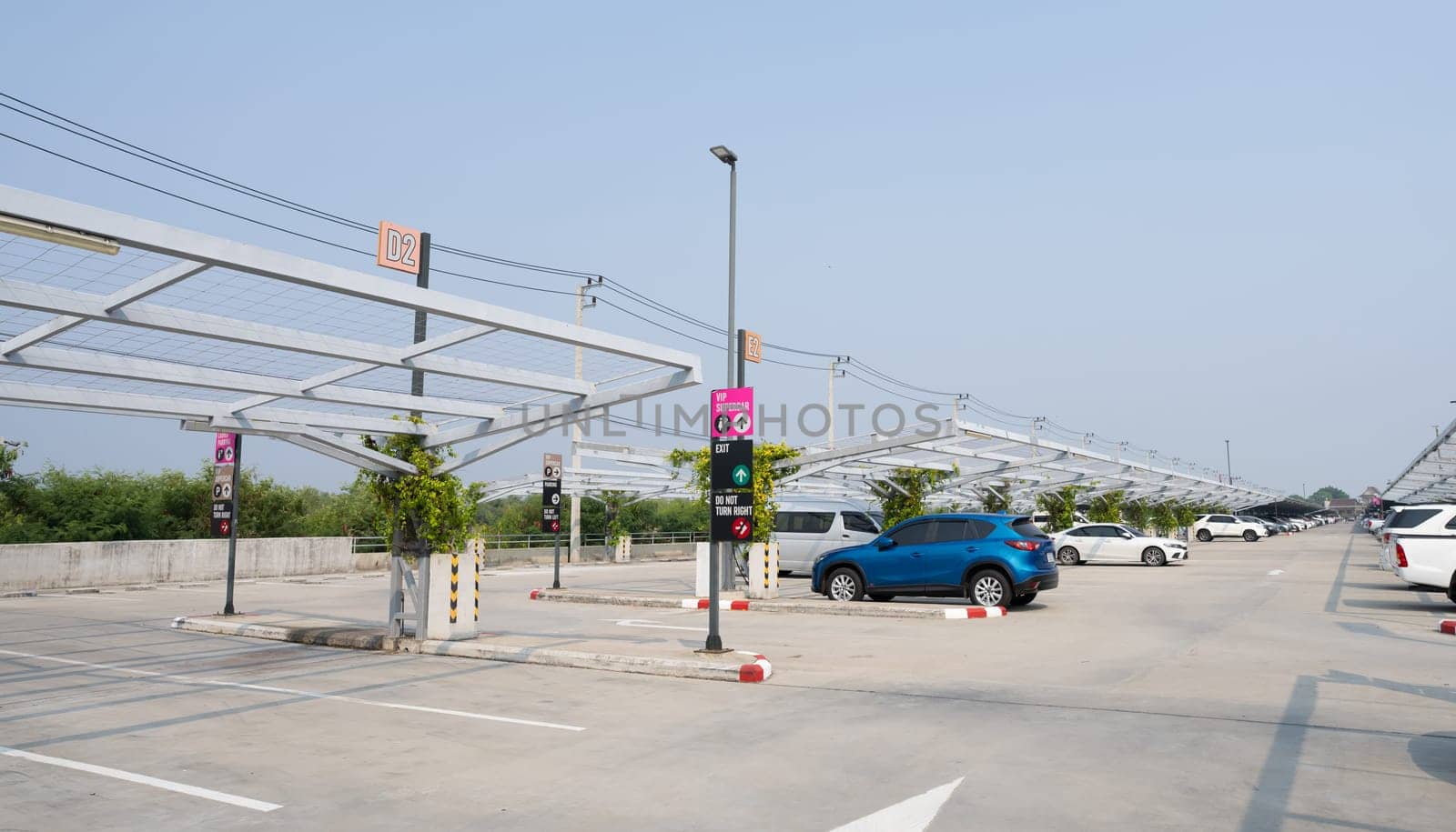 Concrete car parking lot with empty space. Private car park for customer service. Parking zone on a sunny day. Outdoor parking lot of shopping mall. Outdoor car parking lot with green climbing plant. 