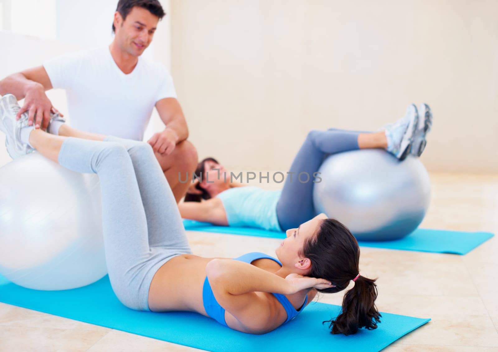 Personal trainer, pilates and help woman with ball, balance and posture with training advice, fitness and gym. Man, exercise and helping women in class with stretching, wellness or workout on floor.