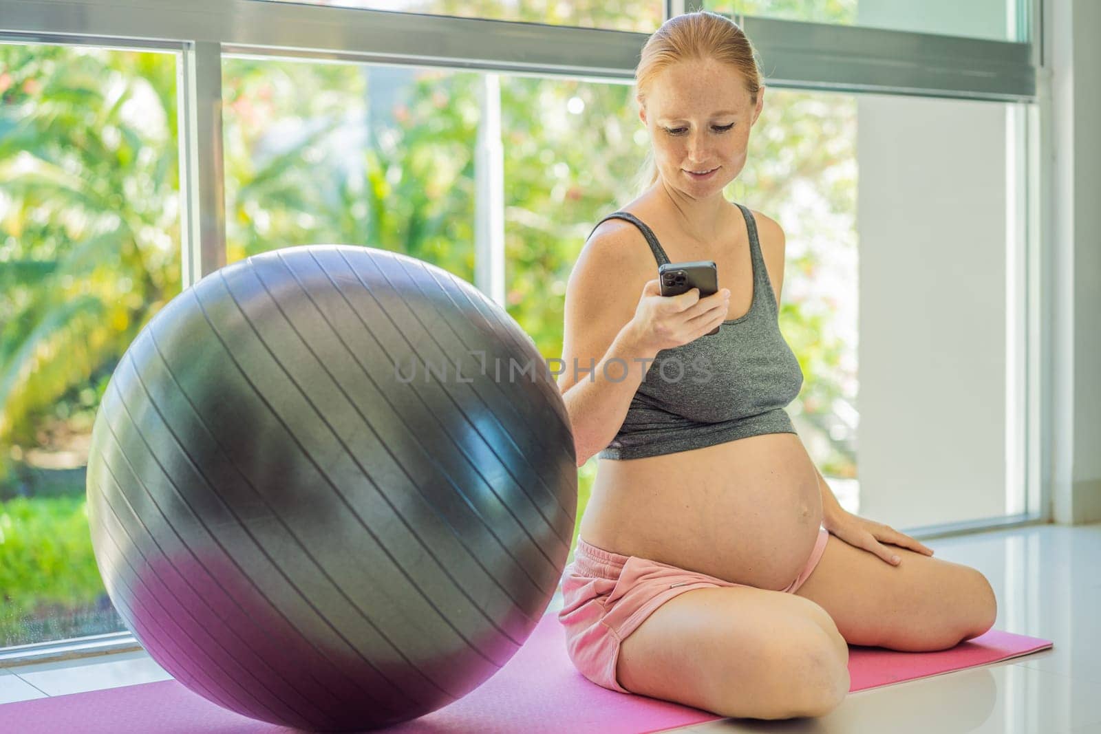 Beautiful pregnant woman texting on smartphone during sports training by galitskaya