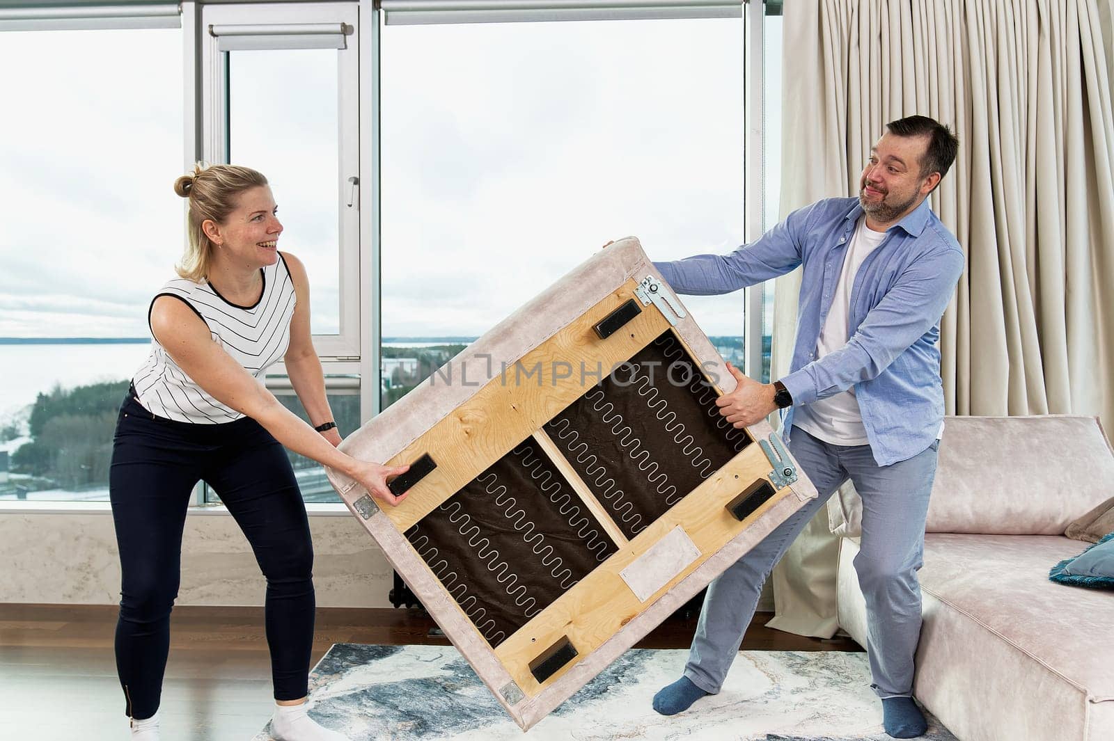 family rearranging furniture. Happy couple moving furniture in new apartment. Moving day, happy buyers. Positive smiling young couple moving furniture