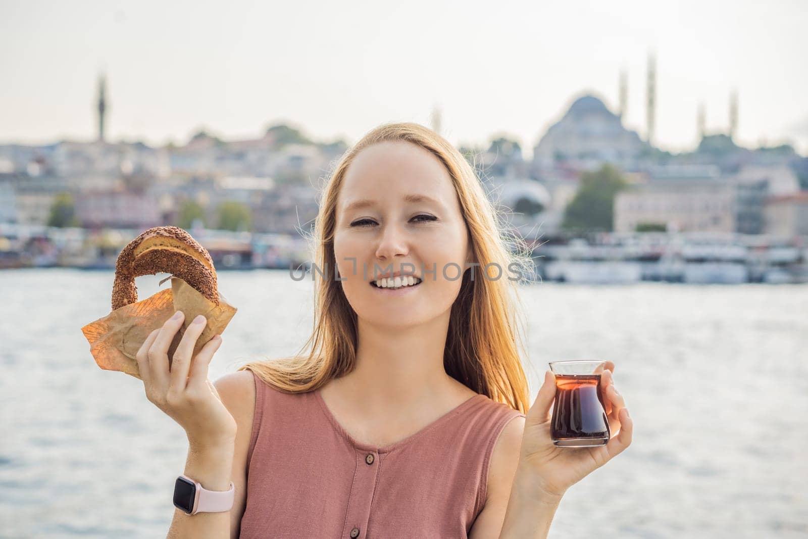 Woman in Istanbul having breakfast with Simit and a glass of Turkish tea. Glass of Turkish tea and bagel Simit against golden horn bay in Istanbul, Turkey. Turkiye.