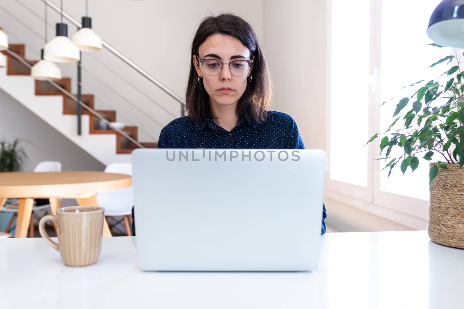 Young Caucasian woman with glasses working with laptop at home. Female freelancer using computer at office. by Hoverstock