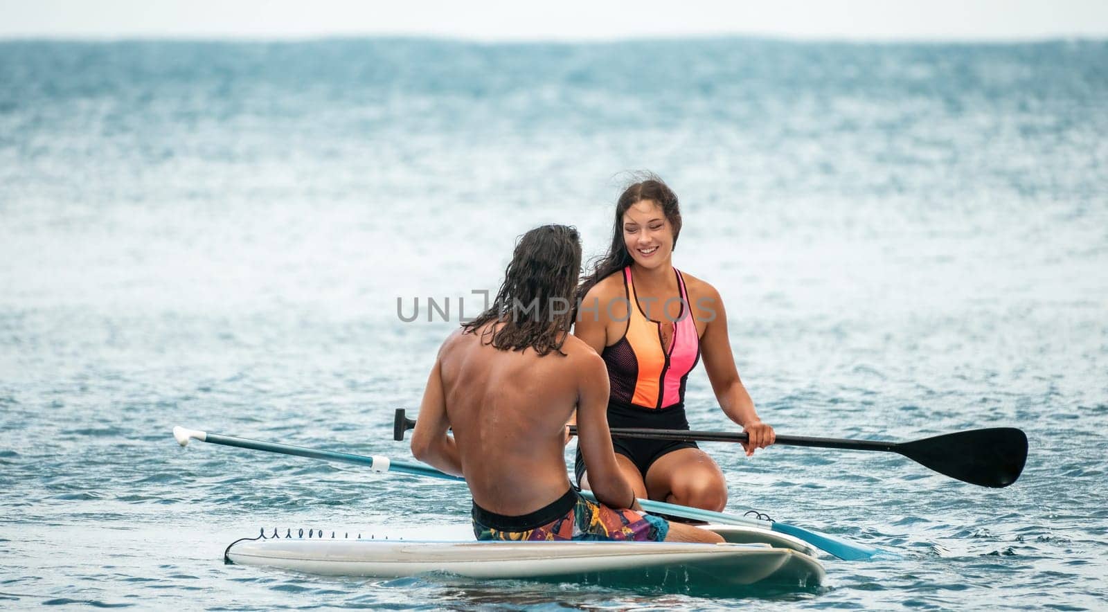 Sea woman and man on sup. Silhouette of happy young woman and man, surfing on SUP board, confident paddling through water surface. Idyllic sunset. Active lifestyle at sea or river